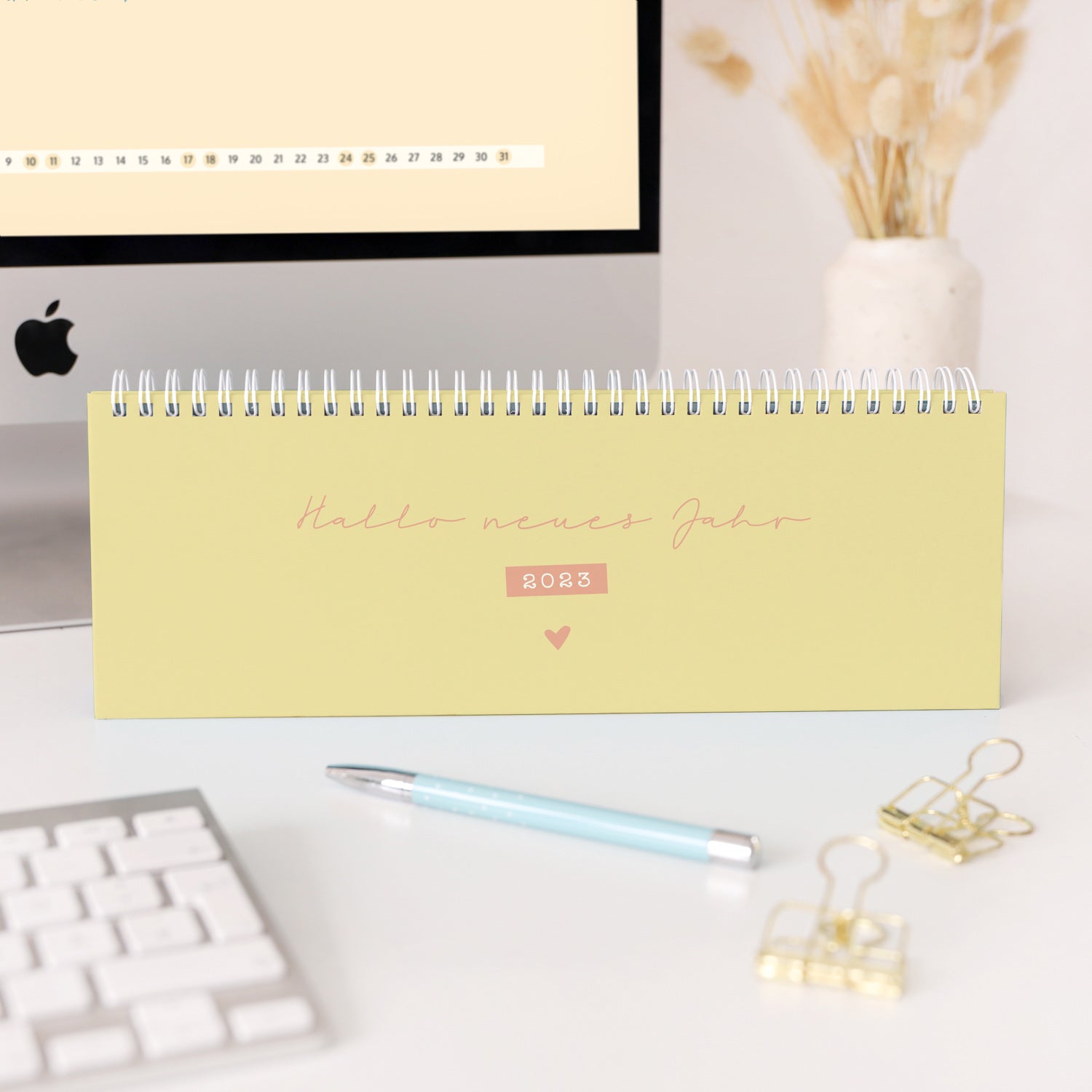 Kalender mit der Aufschrift "Hallo neues Jahr 2023" steht auf einem Schreibtisch mit einem Stift und Büroklammern.