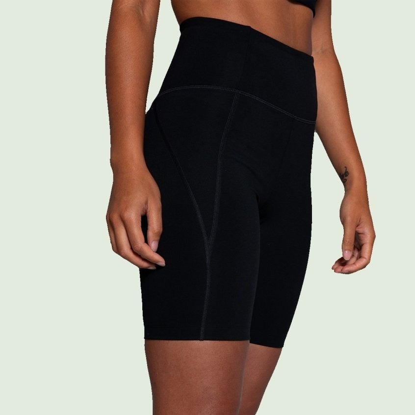 Person in schwarzer Sportshorts vor einem hellen Hintergrund.
