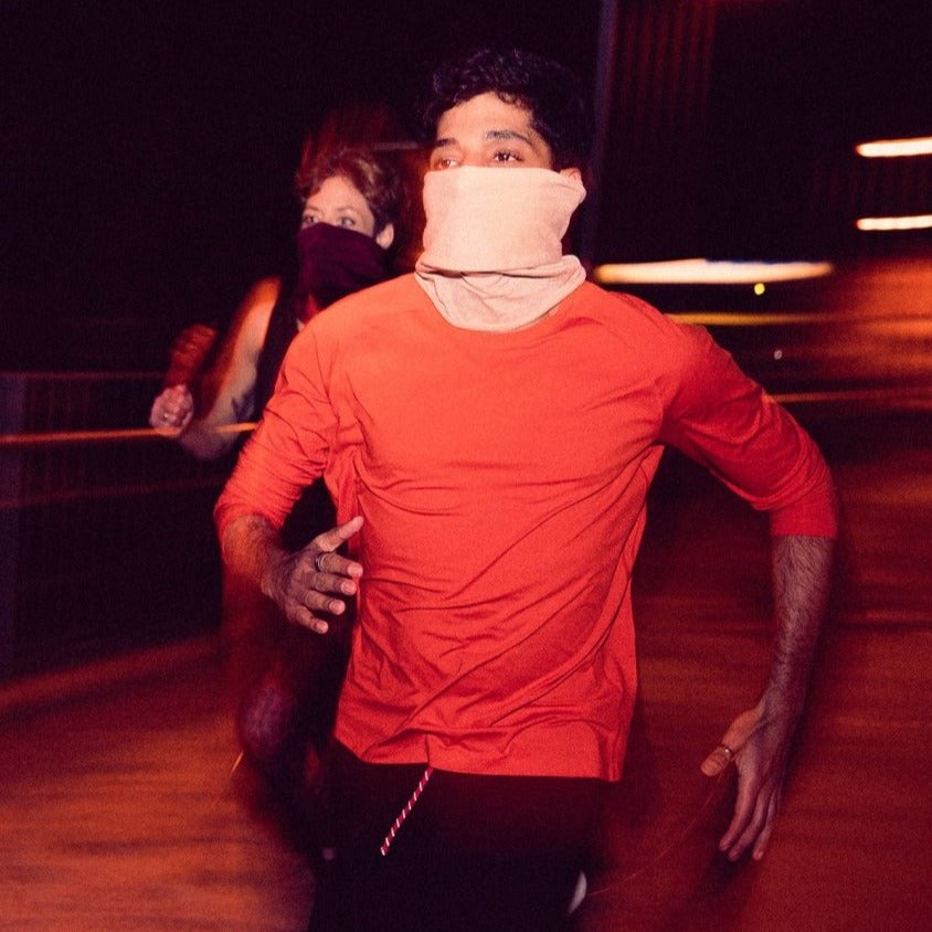 Zwei maskierte Personen rennen bei Nacht durch einen Tunnel, beleuchtet von orangenem Licht.