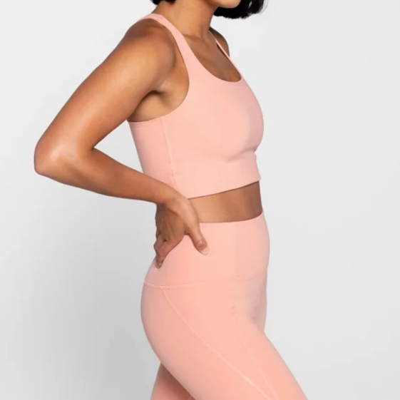 Person in peach-colored athletic wear stands sideways against a white background, hand on hip.