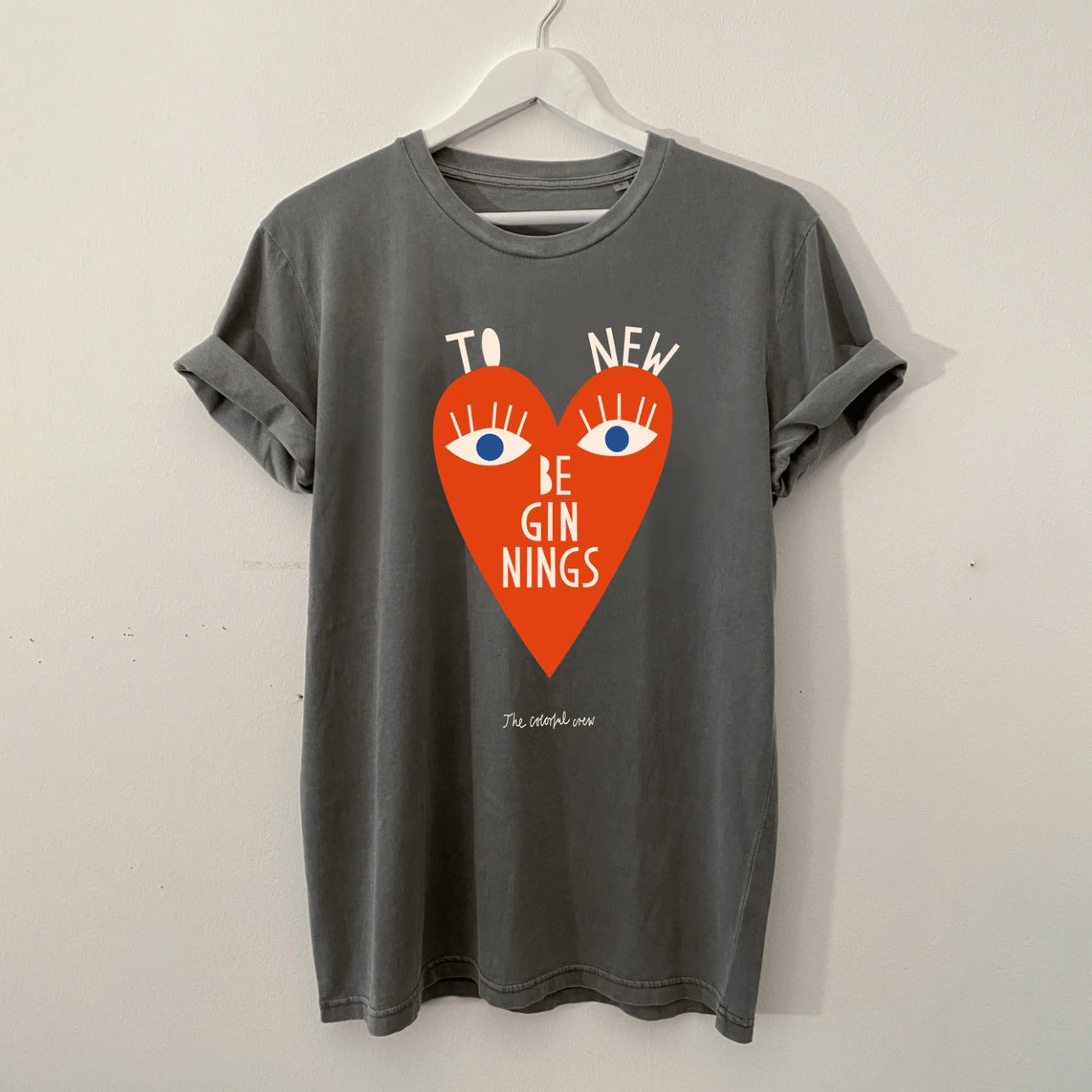 Graues T-Shirt mit einem roten Herzmotiv, auf dem "To New Beginnings" und zwei blaue Augen abgebildet sind.