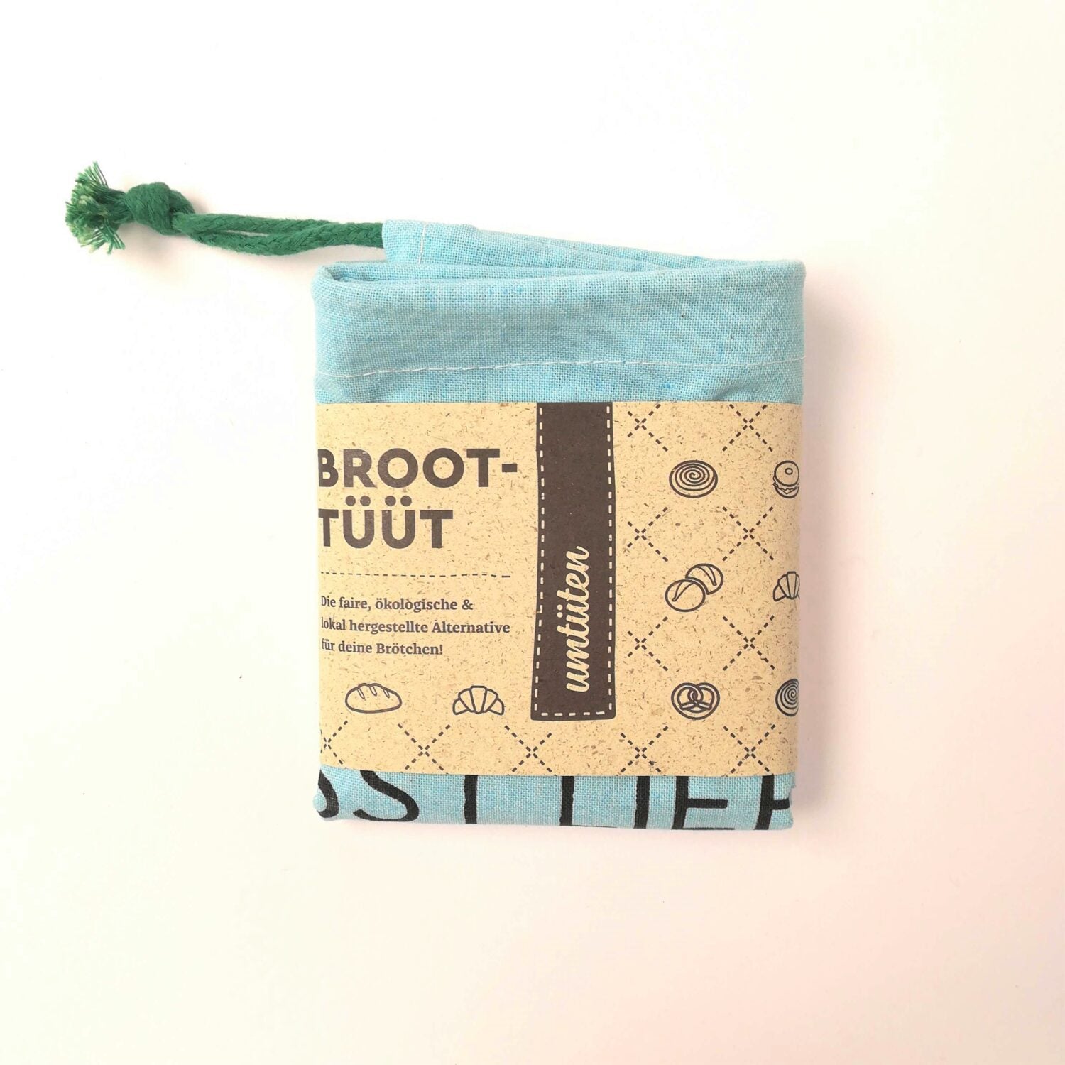Ein türkisfarbener Stoffbeutel mit grünem Zugband und brauner Papierbanderole, bedruckt mit Brotmotiven und Text.