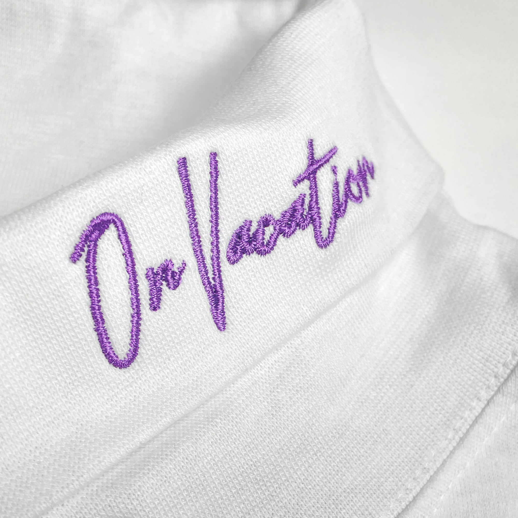 Lila gesticktes "On Vacation" auf weißem Stoff.