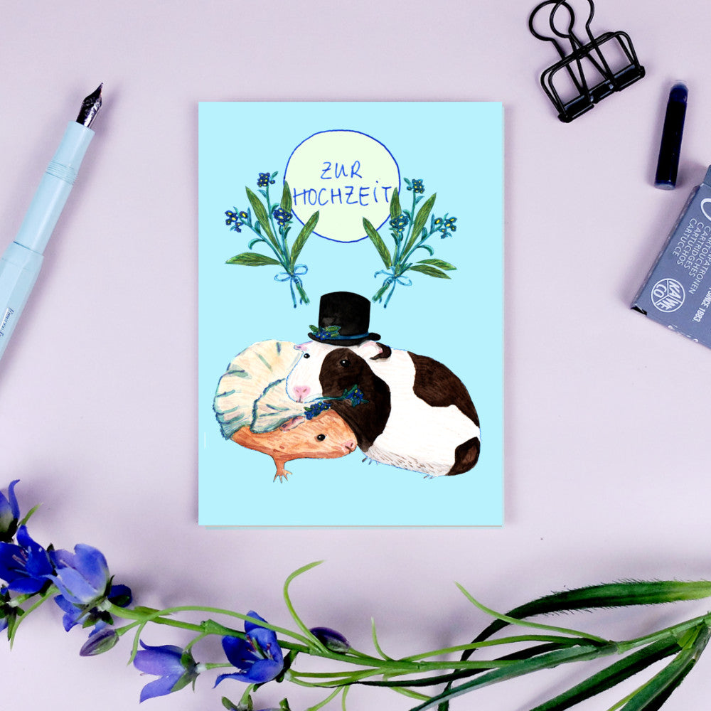 Postkarte mit zwei Meerschweinchen in Hochzeitskleidung, umgeben von Blumen und der Aufschrift "Zur Hochzeit".