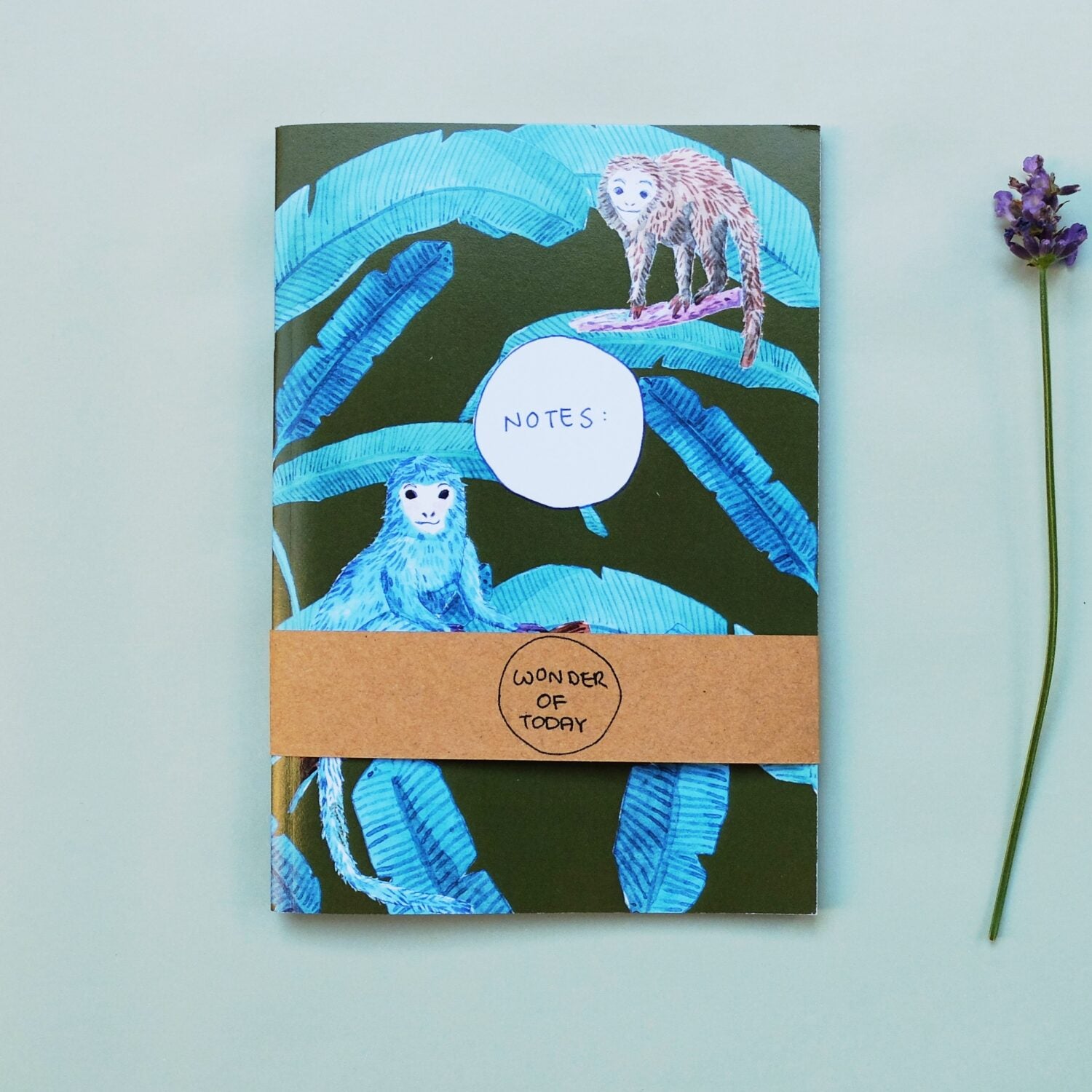 Ein Notizbuch mit Affen- und Blattdesign auf dem Cover, daneben liegt ein kleiner Lavendelzweig.