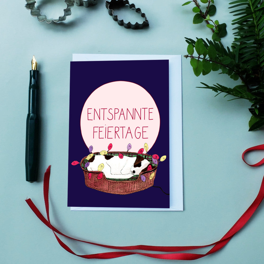 Weihnachtskarte mit einem Hund in einem Korb voller Lichter, dazu der Text "Entspannte Feiertage".