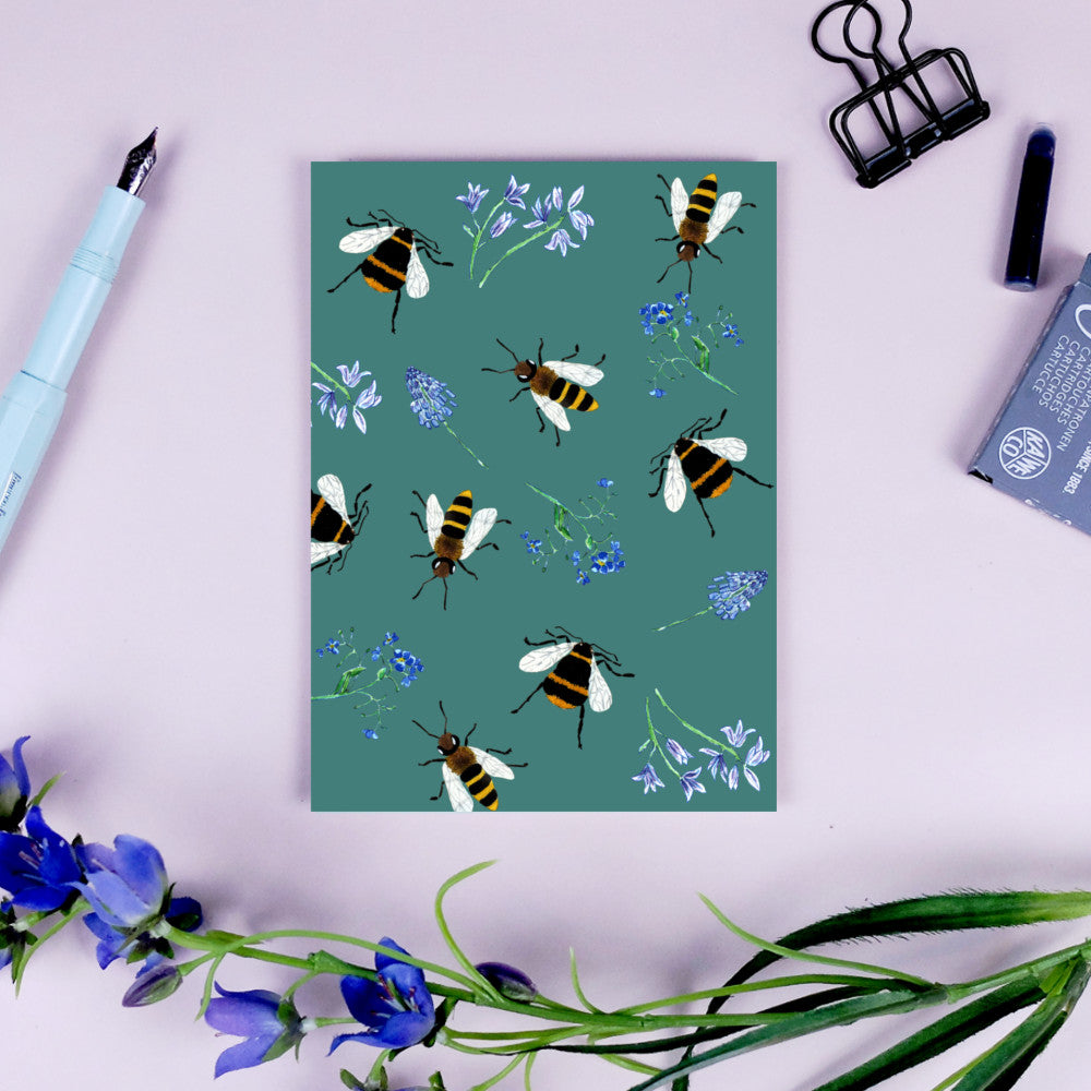 Illustration von Bienen und blauen Blumen auf grünem Hintergrund, umgeben von Stift, Klammer und Blumen.