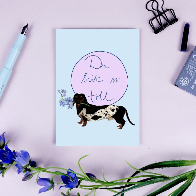 Karte mit Dackel, der eine Blume im Maul hält, umgeben von Büromaterialien. Text: "Du bist so toll."