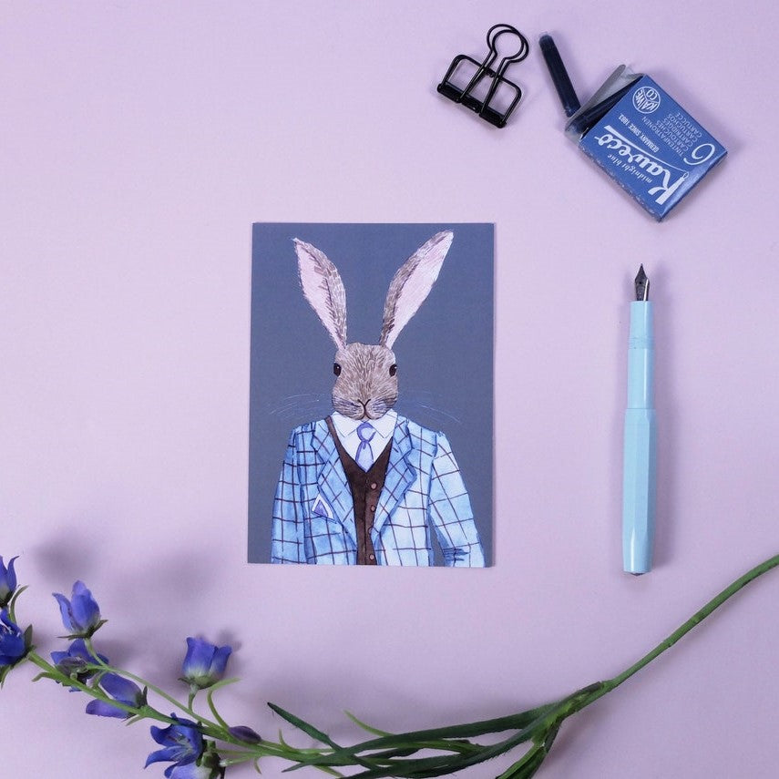 Eine Zeichnung eines Hasen in einem Anzug liegt auf einem rosa Hintergrund, umgeben von einem Stift und Blumen.