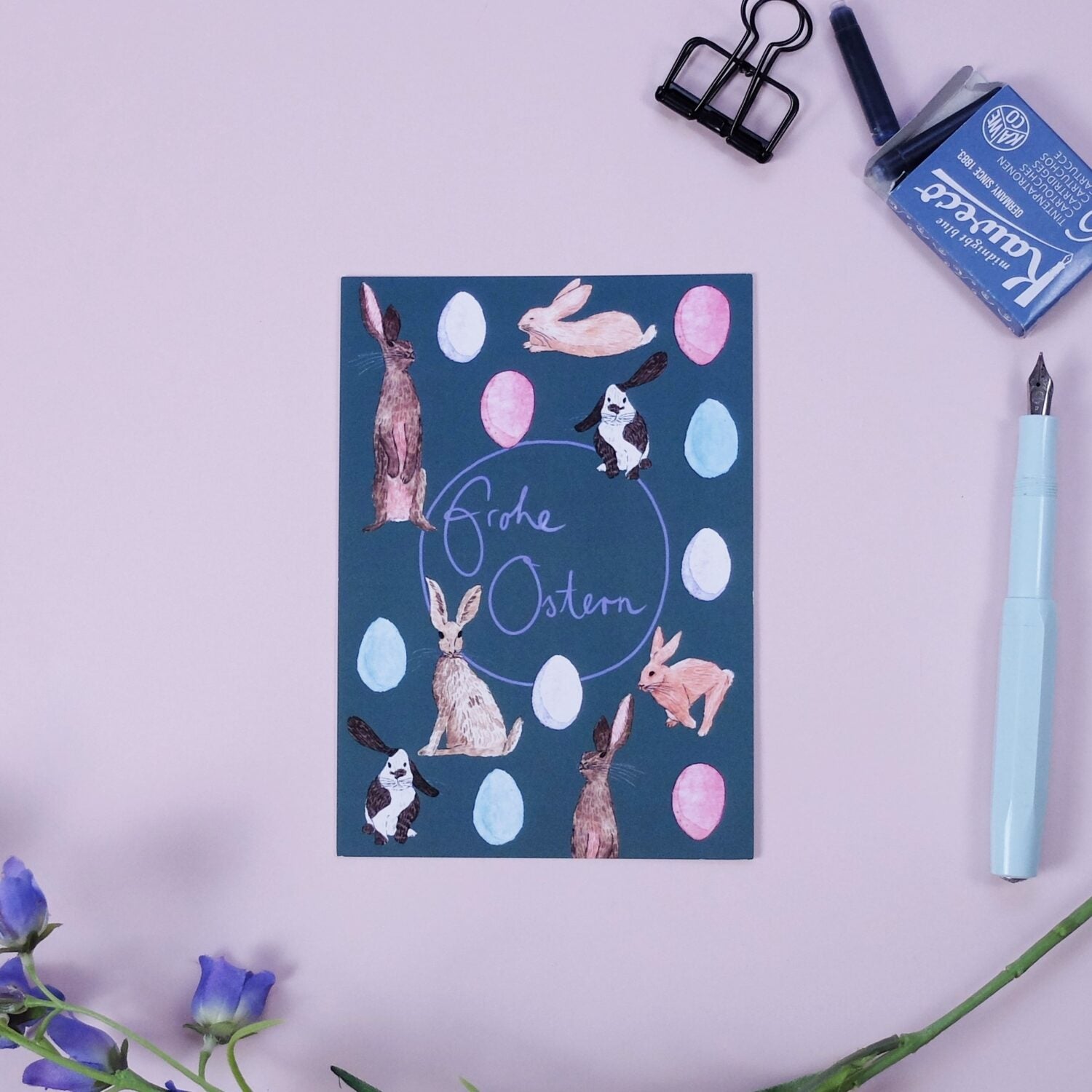 Osterkarte mit Hasen und Eiern, darauf steht "Frohe Ostern", daneben ein Stift, Klammer und Tintenpatronen.