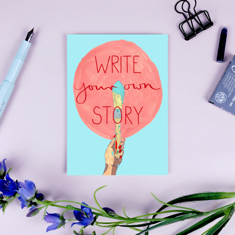 Eine Karte mit der Aufschrift "Write your own story" in einem roten Kreis, umgeben von Schreibzeug und Blumen.