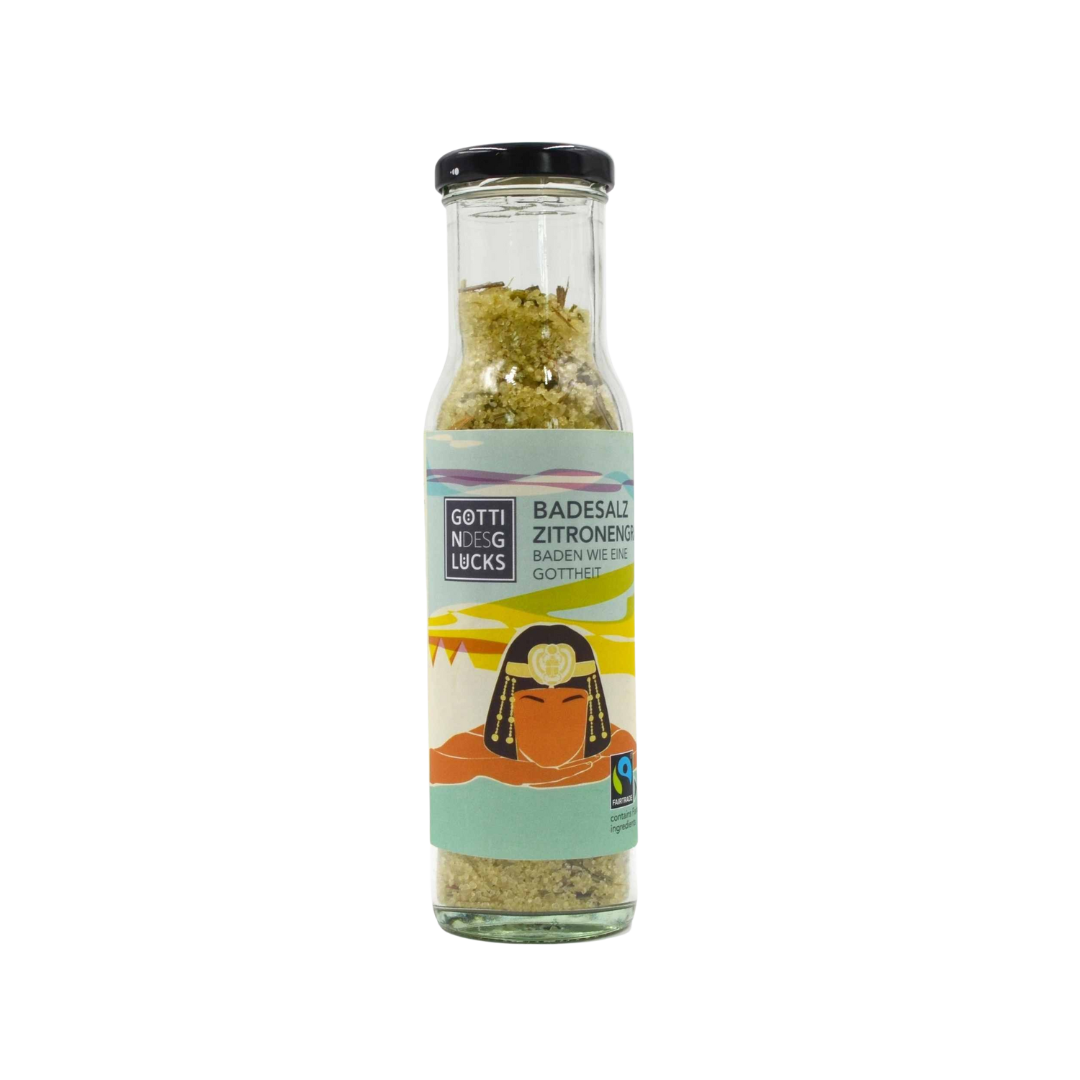 Eine Glasflasche mit schwarzem Deckel, die Badesalz enthält. Das Etikett trägt die Aufschrift Badesalz Zitrone und zeigt die Abbildung einer badenden Person mit Bergen und einem Sonnenuntergang im Hintergrund.