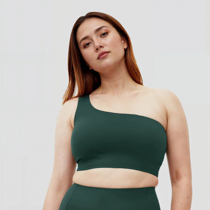 Eine Frau mit langen braunen Haaren trägt ein dunkelgrünes, schulterfreies Crop-Top und eine passende Hose und steht vor einem schlichten, hellen Hintergrund. Sie blickt selbstbewusst in die Kamera.