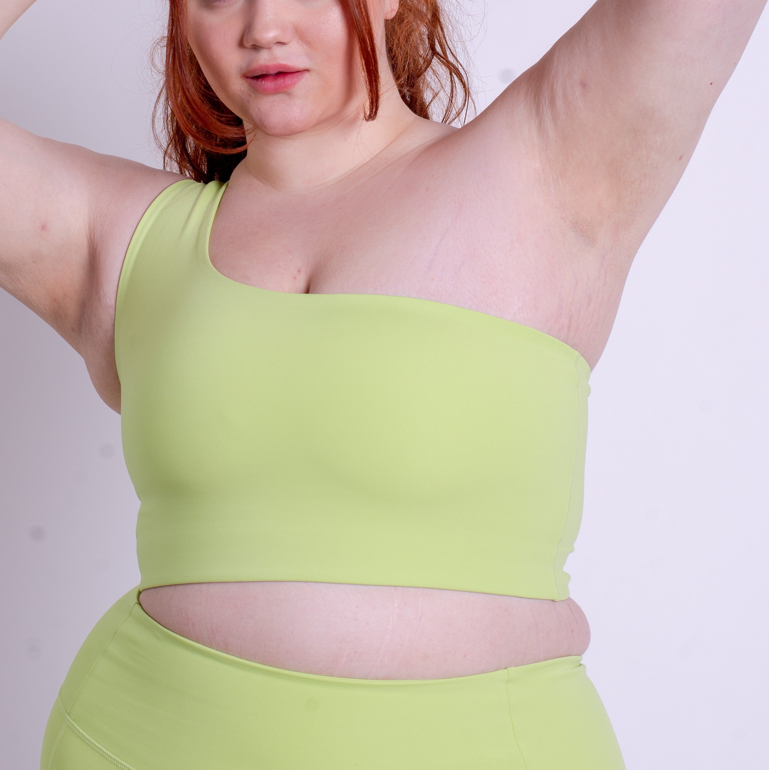 Eine Person mit langen roten Haaren posiert mit einem erhobenen Arm und trägt ein hellgrünes, schulterfreies Crop-Top und eine passende Hose mit hoher Taille. Das Bild ist so beschnitten, dass ihr Oberkörper und ein Teil ihres Gesichts zu sehen sind.