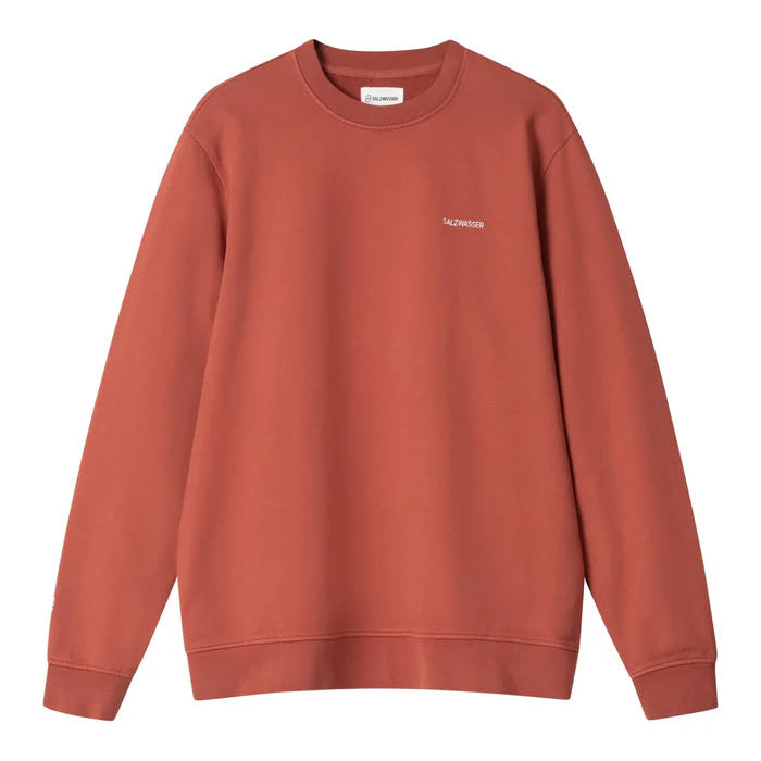 Ein schlichtes, langärmeliges, rostfarbenes Sweatshirt mit Rundhalsausschnitt und einem kleinen weißen Logo auf der linken Brust, das keine anderen sichtbaren Muster oder Motive aufweist.