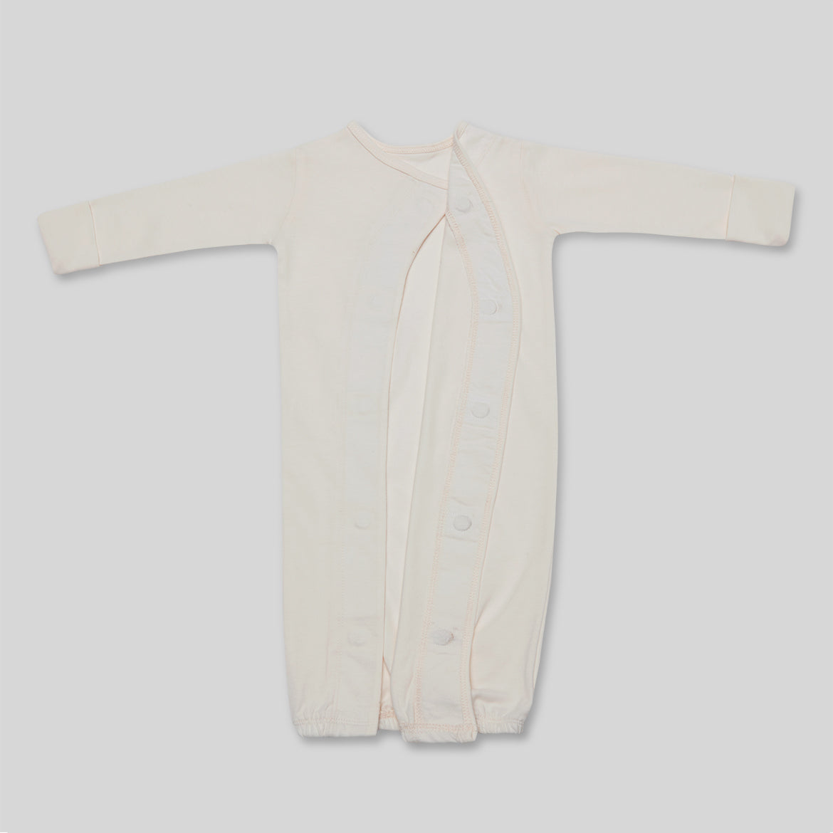 Ein cremefarbener Babystrampler mit langen Ärmeln und Knöpfen an der Vorderseite liegt auf einer grauen Fläche.