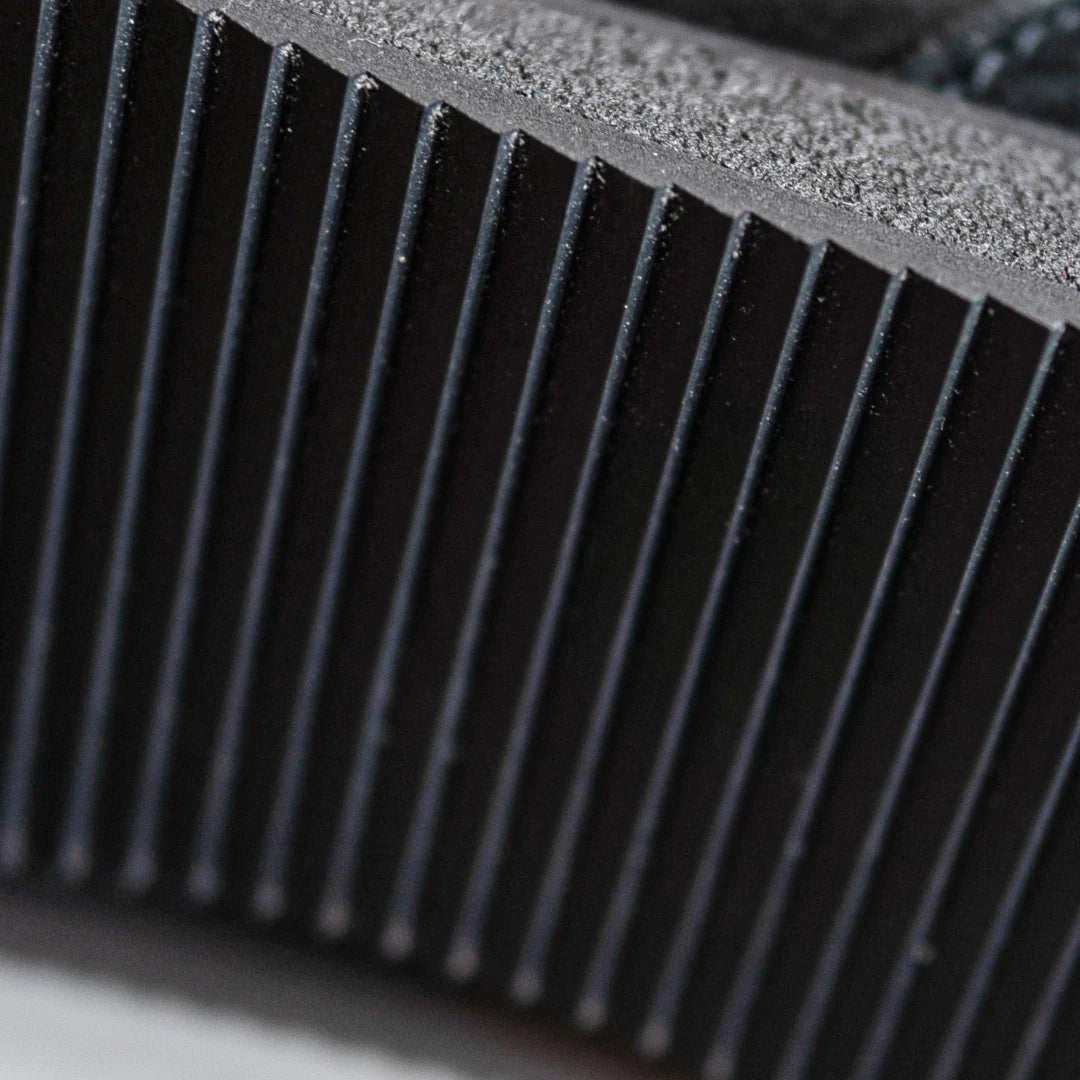 Nahaufnahme einer schwarzen gerippten Gummischuhsohle mit tiefen vertikalen Rillen, die die Textur und das Muster des Materials zeigen.