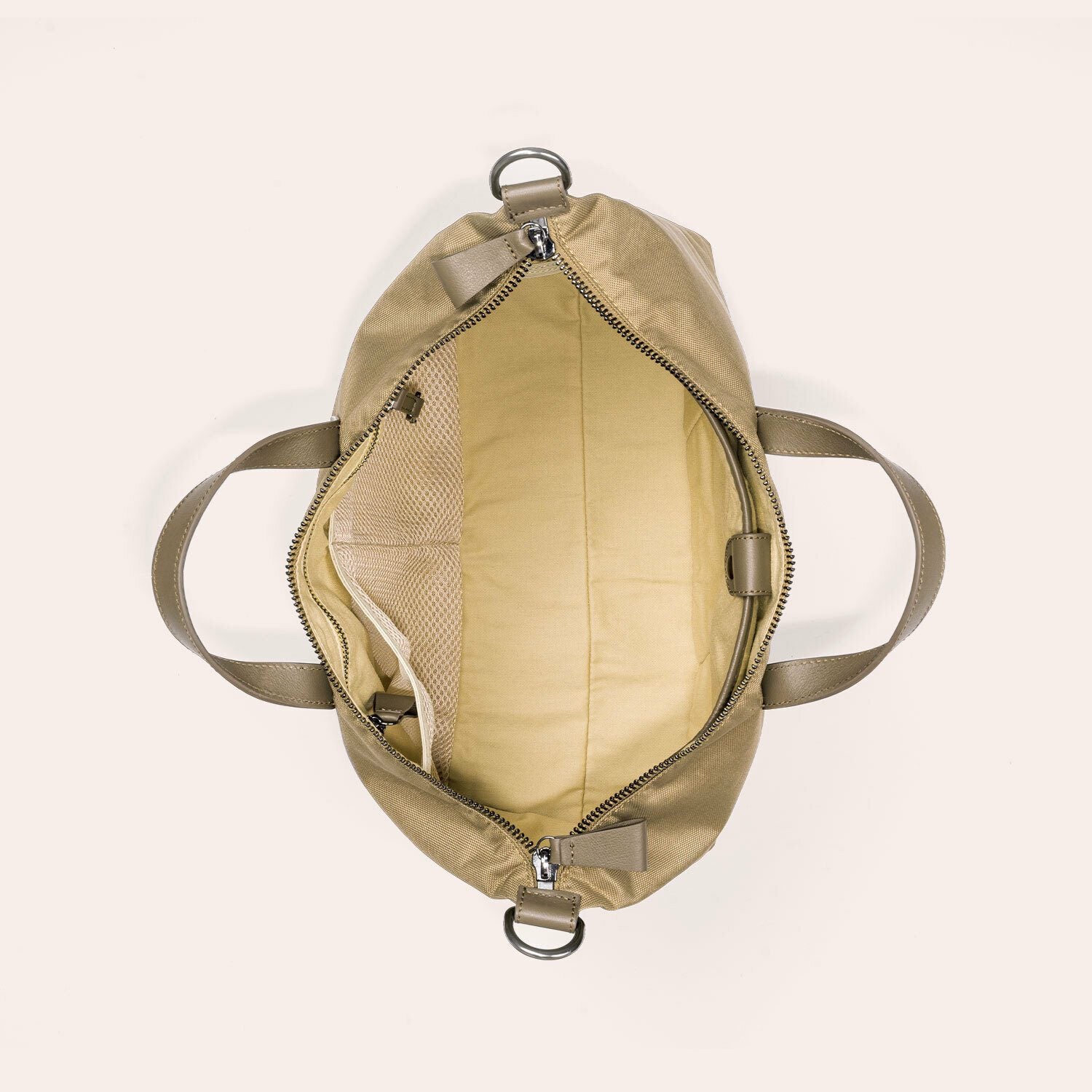 Draufsicht auf eine offene beigefarbene Tragetasche mit zwei Henkeln, die einen geräumigen Innenraum, eine Netztasche auf der einen Seite und eine Reißverschlusstasche auf der anderen Seite offenbart; die Tasche ist leer und ungefüttert.