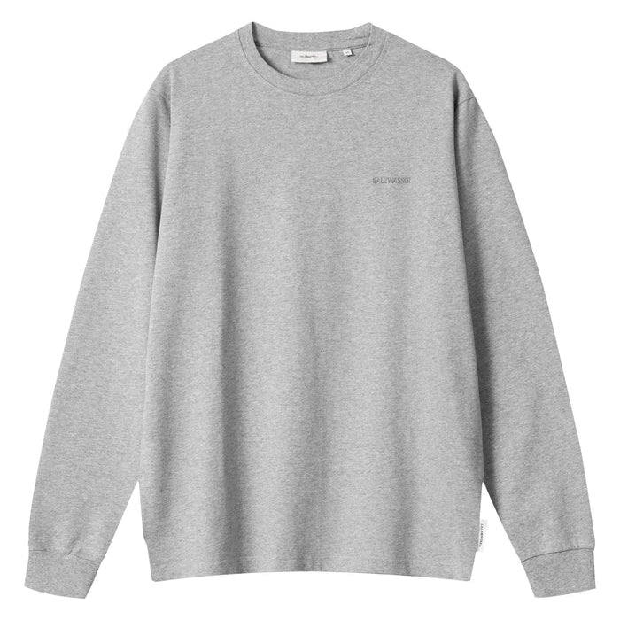 Ein schlichtes graues Langarm-Sweatshirt mit Rundhalsausschnitt, gerippten Bündchen und Saum, mit minimalistischem Text auf der linken Brust und einem kleinen weißen Etikett an der unteren Seitennaht.