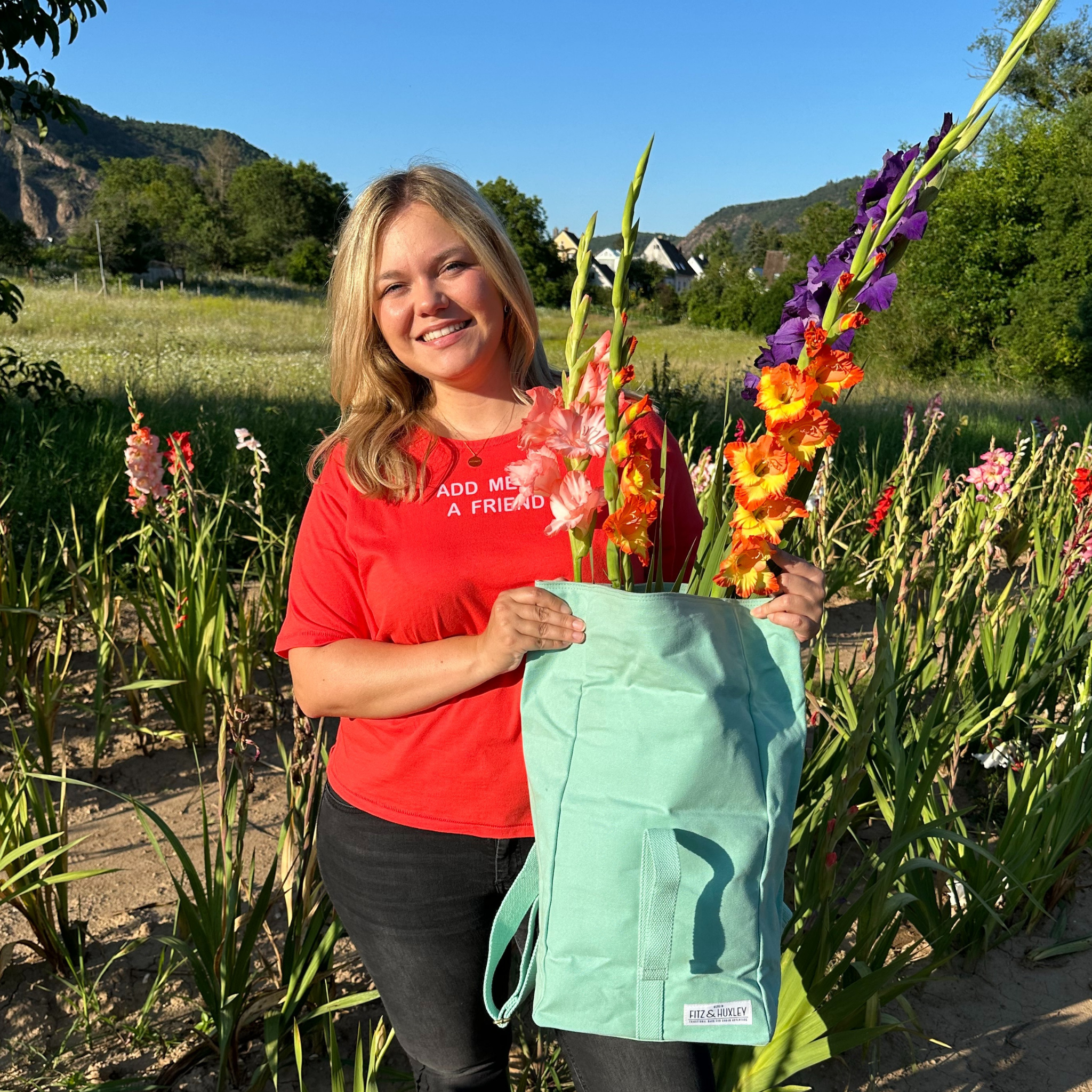 Eine Frau steht auf einem Blumenfeld und hält eine Tasche mit bunten Gladiolen in der Hand.