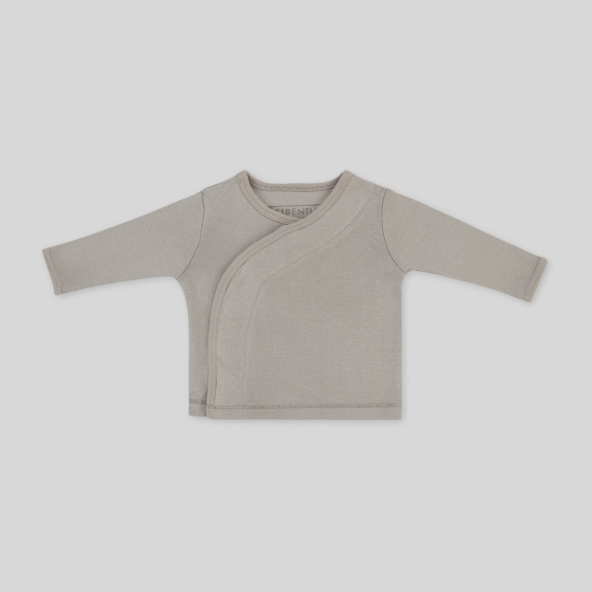 Langärmliges, beiges Babyshirt mit Wickeloptik vor weißem Hintergrund.