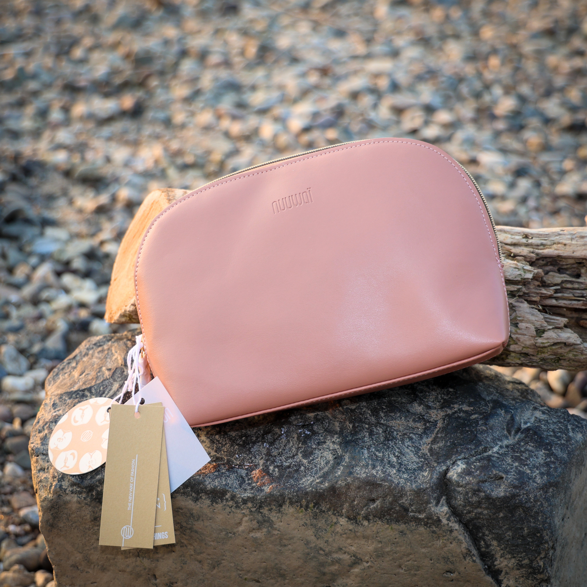 Rosa Ledertasche mit Etiketten, auf einem Stein im Freien liegend.