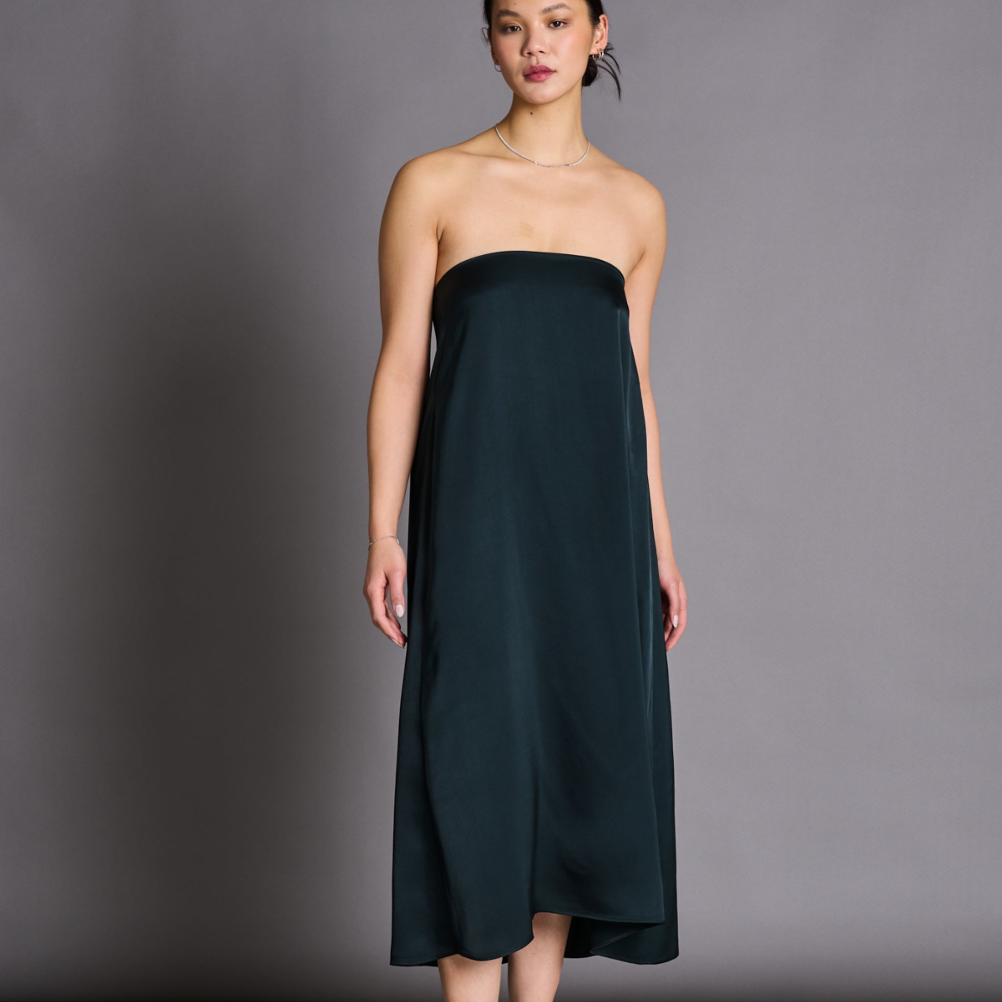 Person in einem schulterfreien, dunklen Kleid vor grauem Hintergrund.