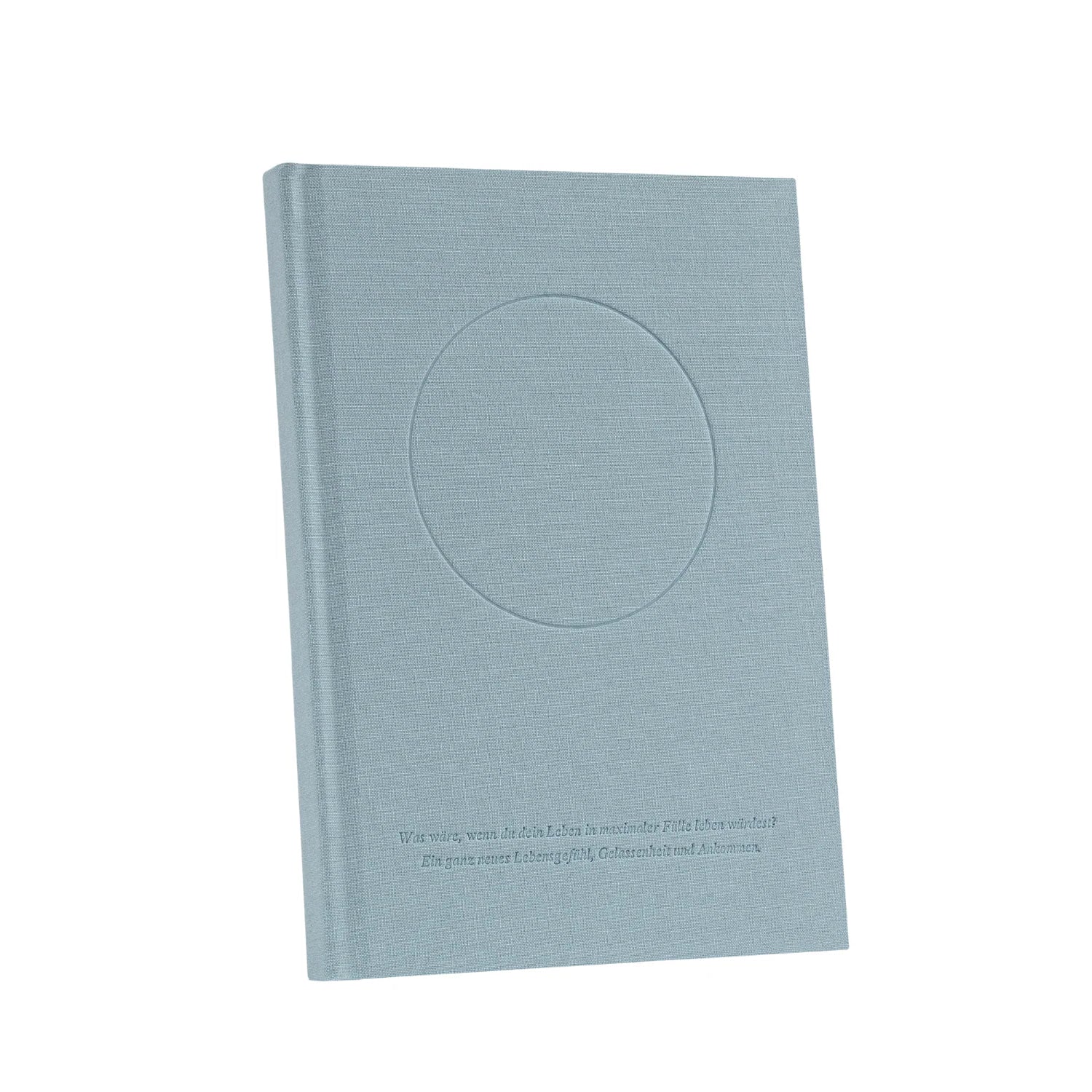 Ein hellblauer Hardcover-Einband mit einer kreisförmigen Vertiefung auf der Vorderseite und einer Zeile mit geprägtem Text in der Nähe des Bodens, der vor einem schlichten weißen Hintergrund steht.
