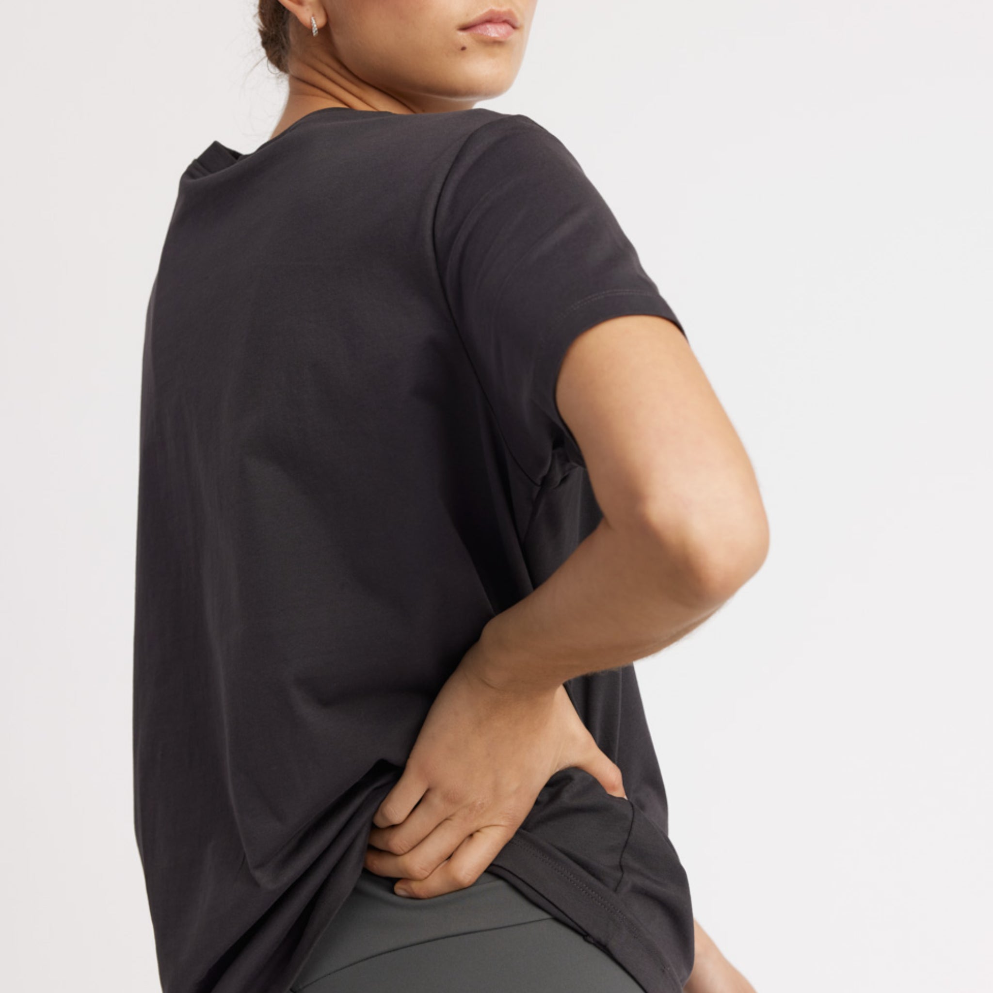 Person in a black T-shirt and gray leggings, seen from the back, with one hand on hip.