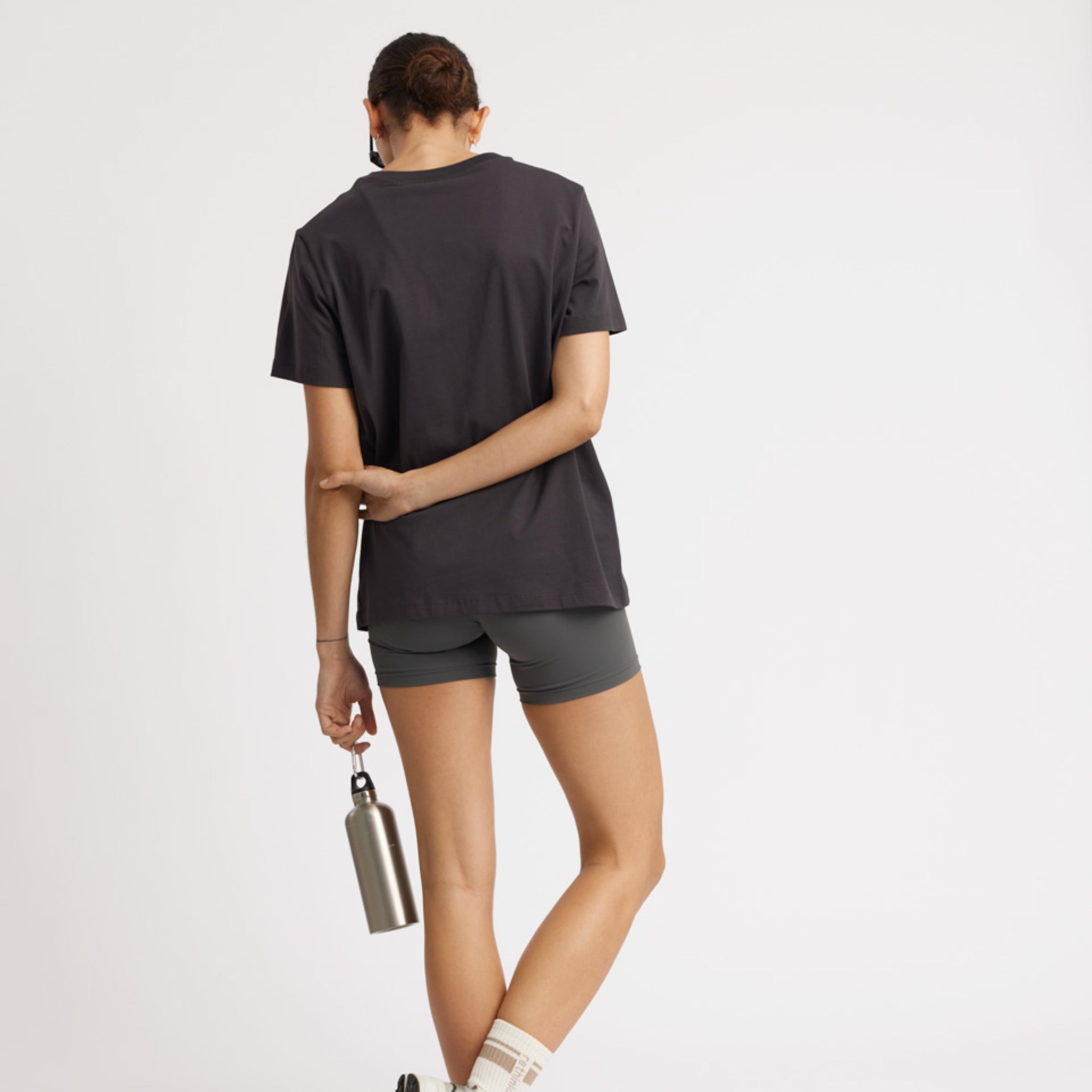 Person von hinten in sportlicher Kleidung hält eine Wasserflasche in der Hand vor einem weißen Hintergrund.