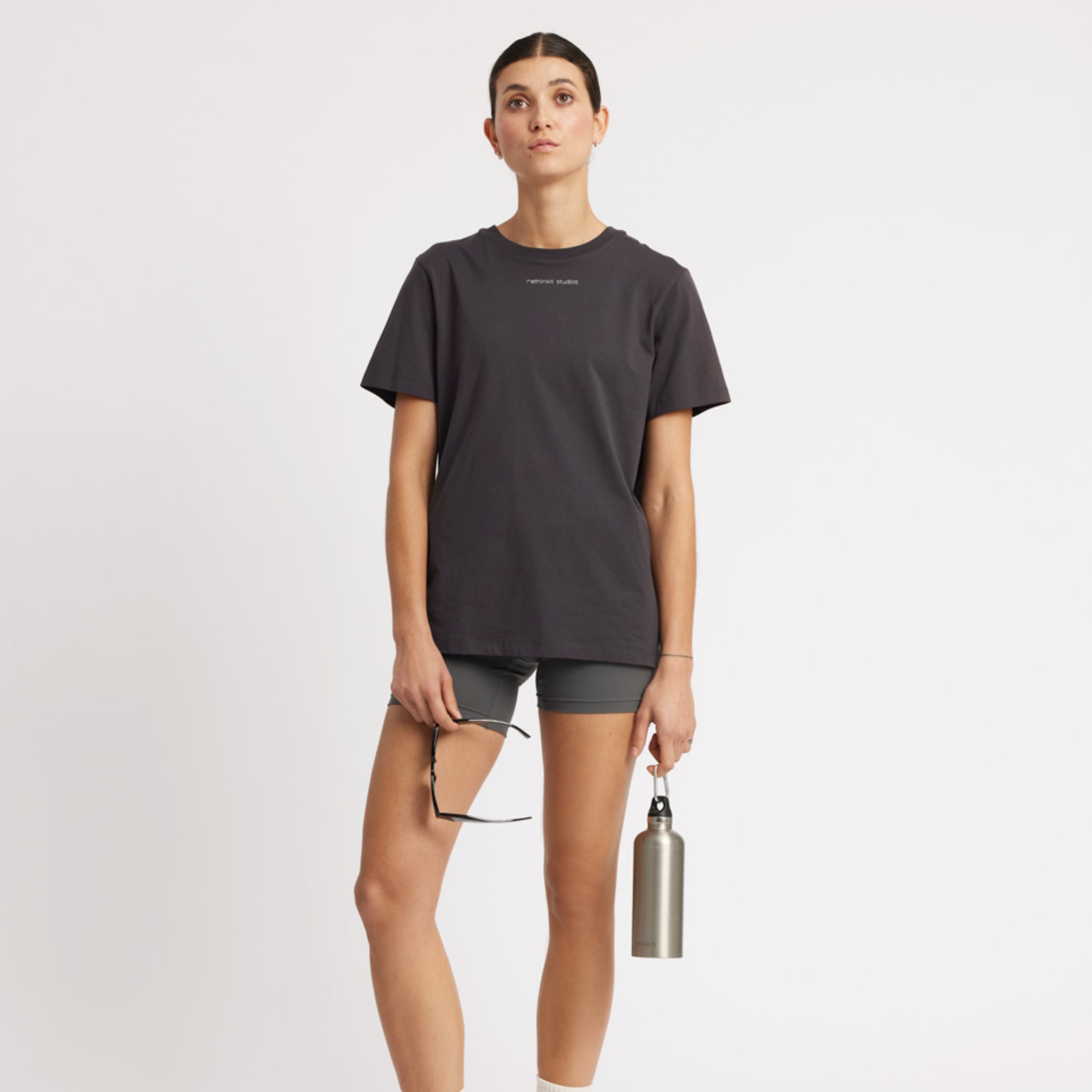 Eine Frau in sportlicher Kleidung hält eine Flasche in einer Hand und eine Sonnenbrille in der anderen.