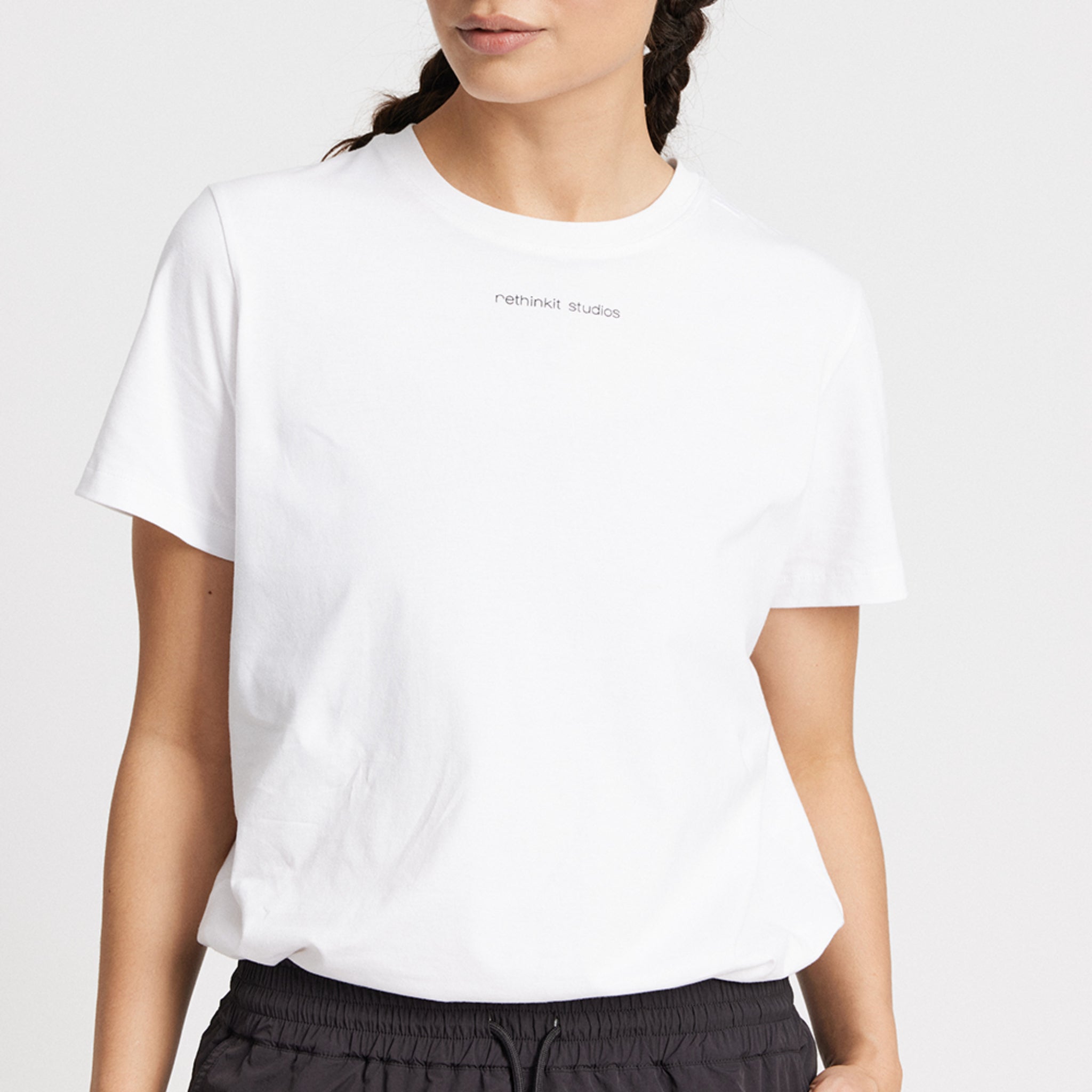 Frau trägt ein weißes Shirt mit "rethinkit studios" Aufschrift und schwarze Hose vor weißem Hintergrund.