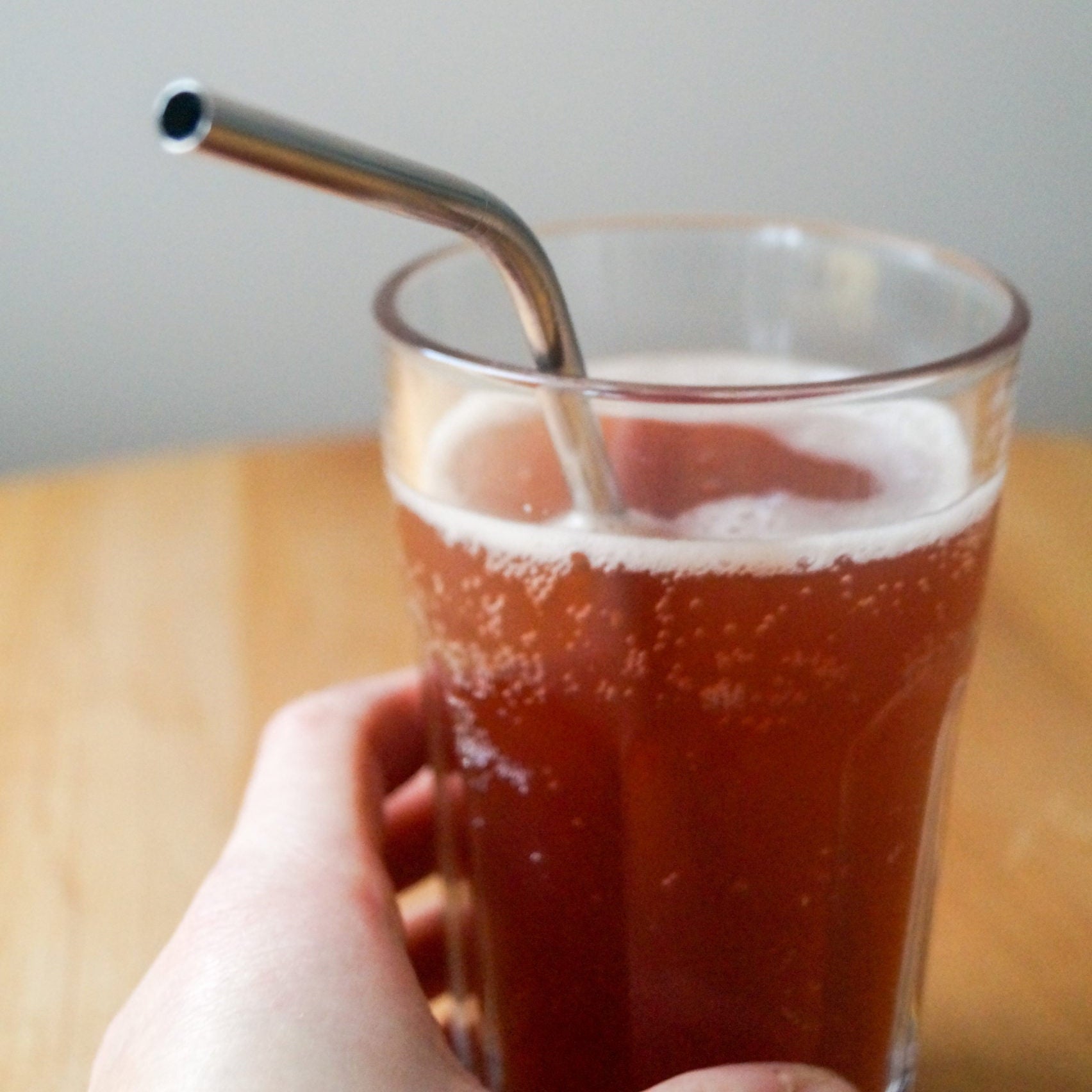 Eine Hand hält ein Glas mit sprudelndem rotem Getränk und einem Metallstrohhalm.
