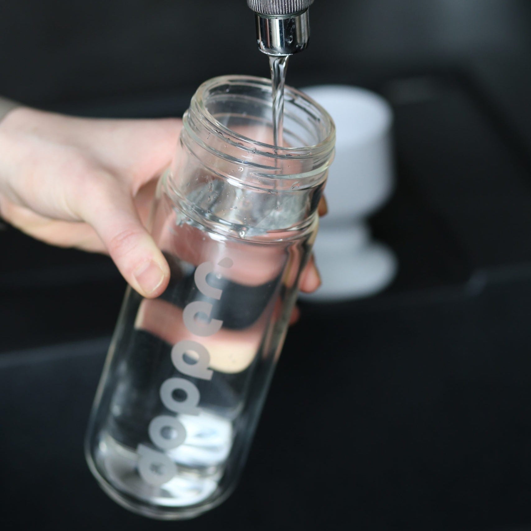 Eine Hand hält eine Glasflasche unter einen Wasserhahn, während Wasser eingefüllt wird.