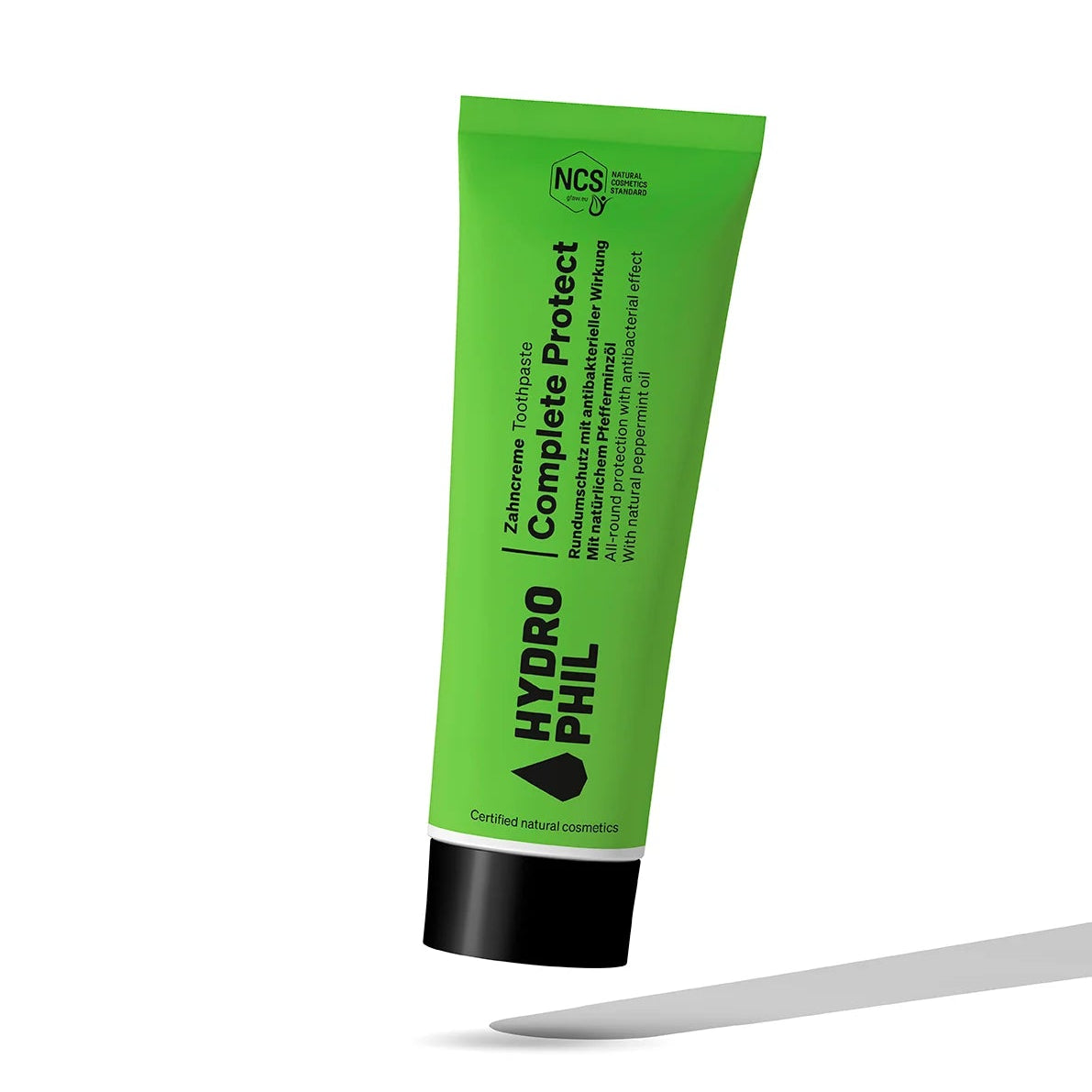 Eine grüne Tube der Zahnpasta Hydrophil Complete Protect steht aufrecht auf einem weißen Hintergrund mit einem grauen Schatten darunter. Das Etikett enthält schwarzen und weißen Text und Zertifizierungssymbole.