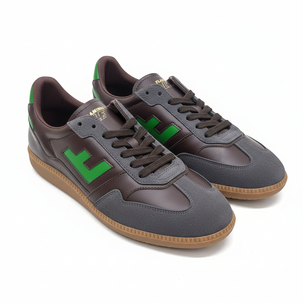 Ein Paar Turnschuhe mit dunkelbraunen, grauen und grünen Akzenten, mit einem grünen F an der Seite, braunen Schnürsenkeln und gummifarbenen Sohlen, die auf einer hellgrauen Oberfläche dargestellt sind.