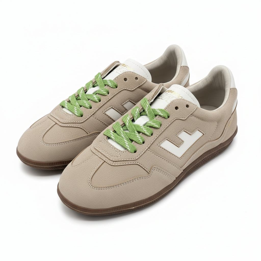 Ein Paar beigefarbene Wildleder-Sneakers mit weißen Akzenten und grünen Schnürsenkeln, mit einem großen weißen "F"-Logo an den Seiten, auf einem grauen Boden.