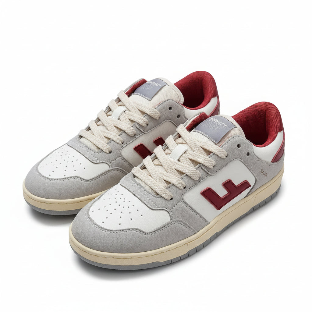 Ein Paar Turnschuhe mit weißem Obermaterial, hellgrauen Wildlederüberzügen, rotem Innenfutter und roten "L"-Logos an den Seiten, die auf einem grauen, strukturierten Boden stehen.