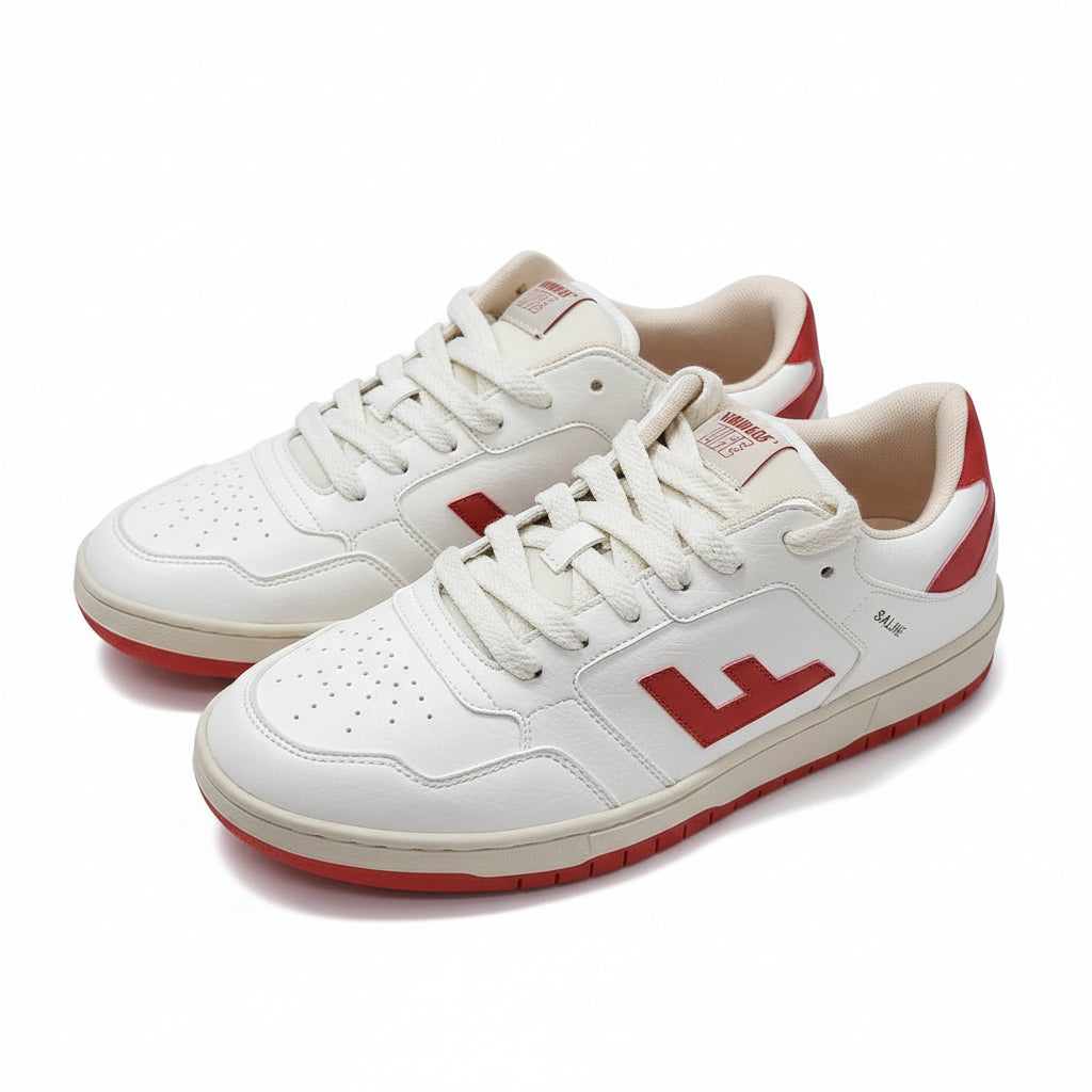 Ein Paar weiße Turnschuhe mit roten Akzenten und einem großen roten E an der Seite, die auf einem grauen Boden stehen. Die Schuhe haben weiße Schnürsenkel und rote Details an der Ferse, Sohle und Zunge.