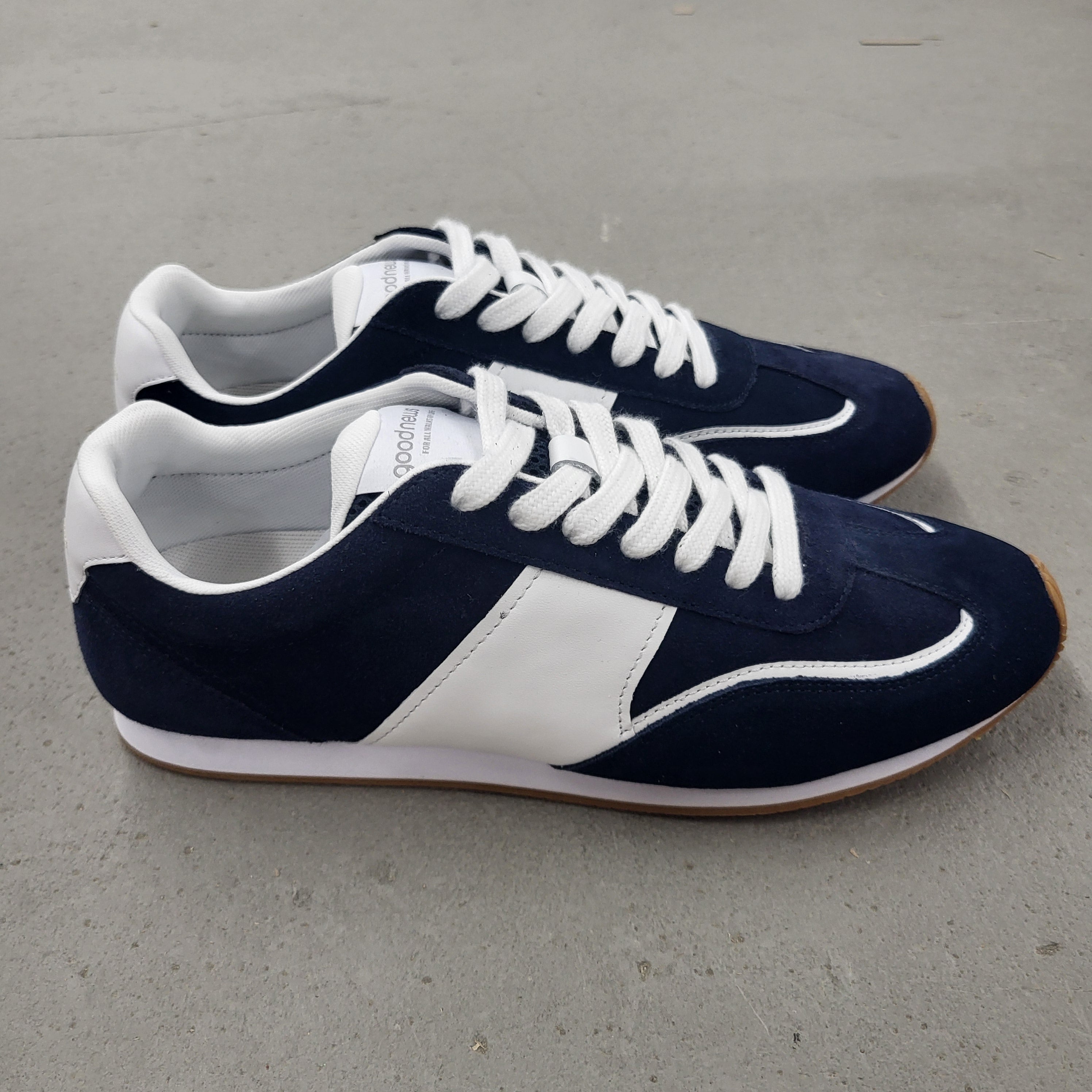 Ein Paar marineblaue und weiße Schnürschuhe mit weißen Sohlen, die nebeneinander auf einer einfarbig grauen Fläche stehen.