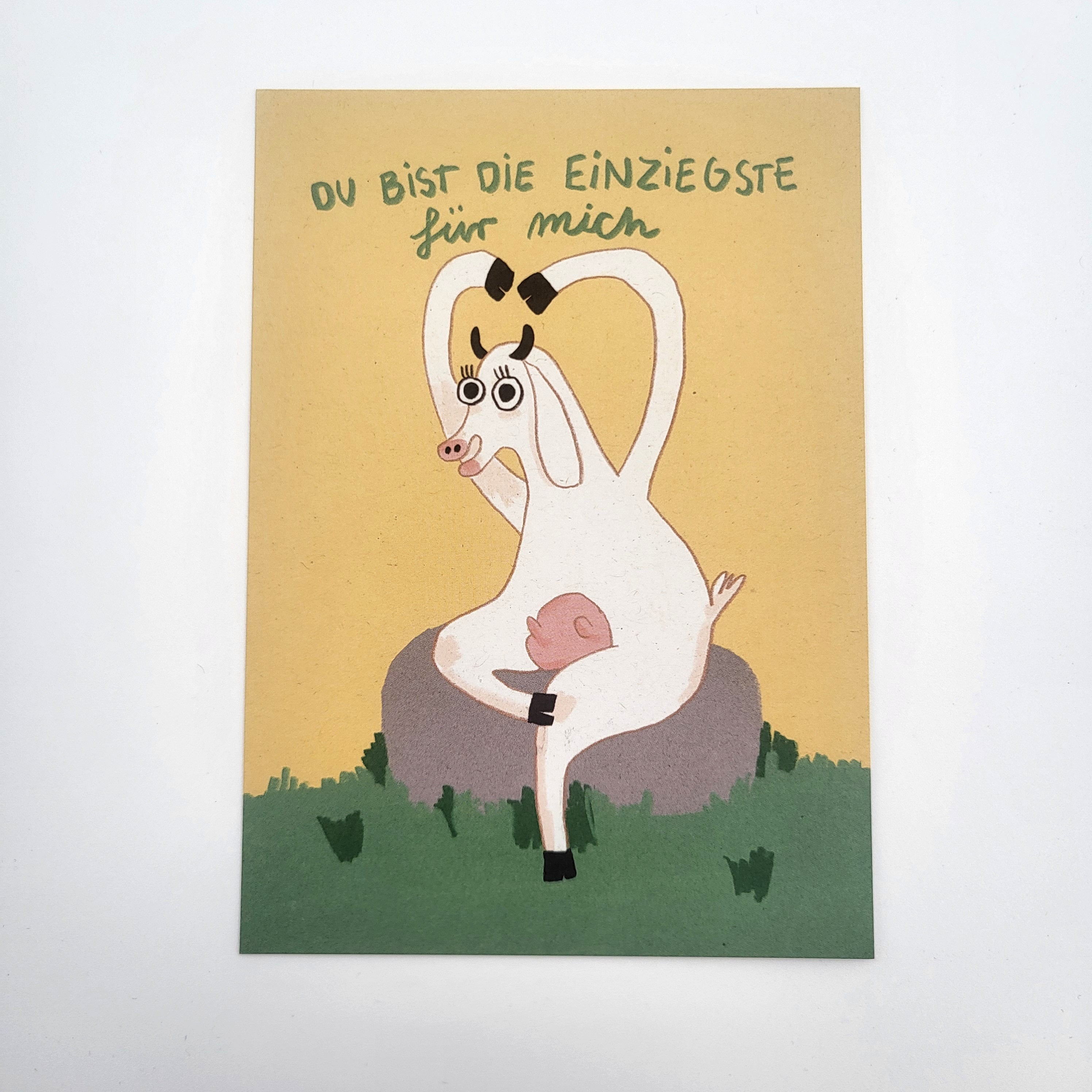 Eine Cartoon-Ziege mit langen Beinen sitzt auf einem Felsen und bildet mit ihren Armen ein Herz. Über ihrem Kopf steht ein deutscher Text: Du bist die Einzigste für mich, was bedeutet: Du bist die Einzige für mich.