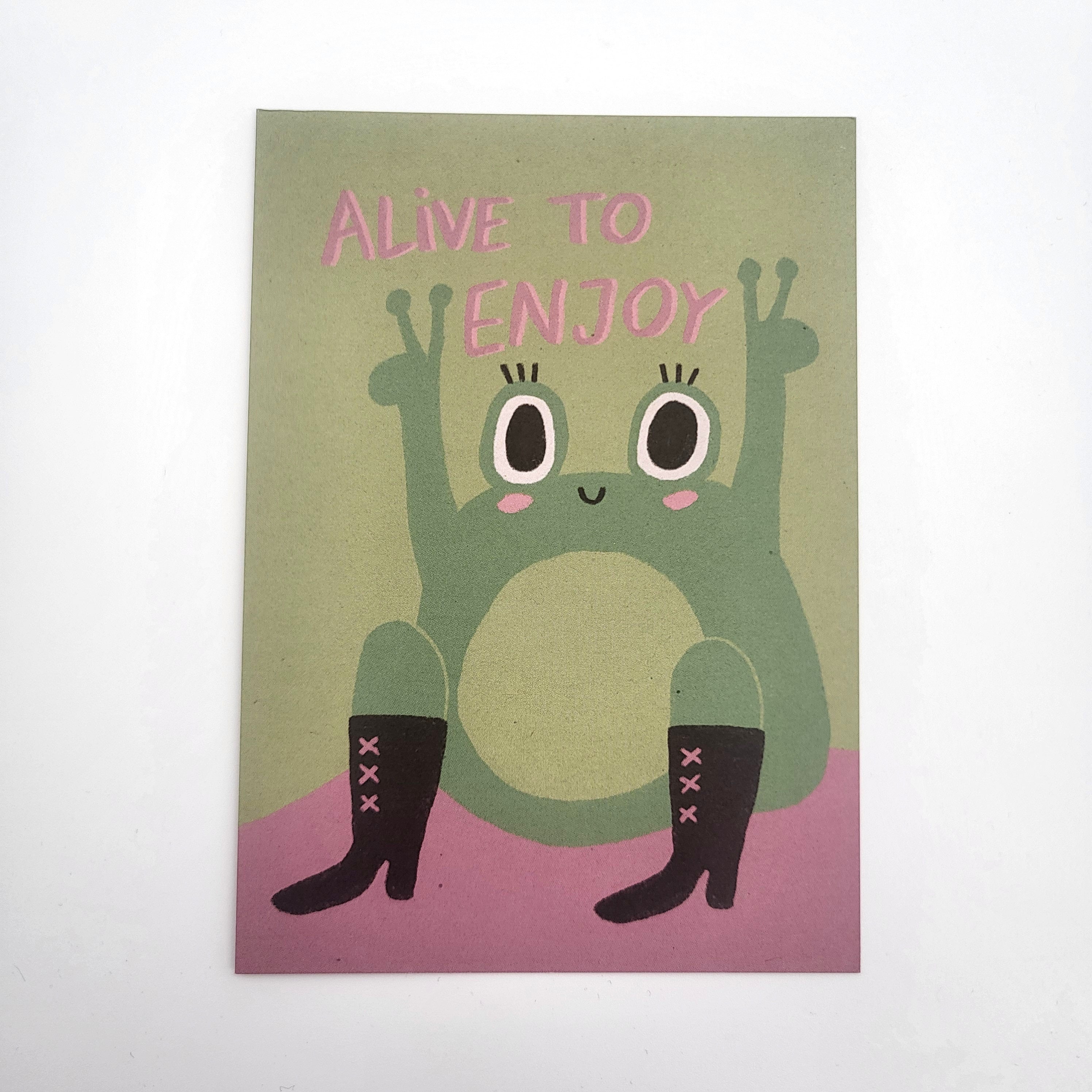 Ein niedlicher Cartoon-Frosch mit großen Augen, der schwarze Stiefel trägt, sitzt mit erhobenen Armen auf einer rosa Fläche. Der Text darüber lautet ALIVE TO ENJOY in rosa Buchstaben auf grünem Hintergrund.