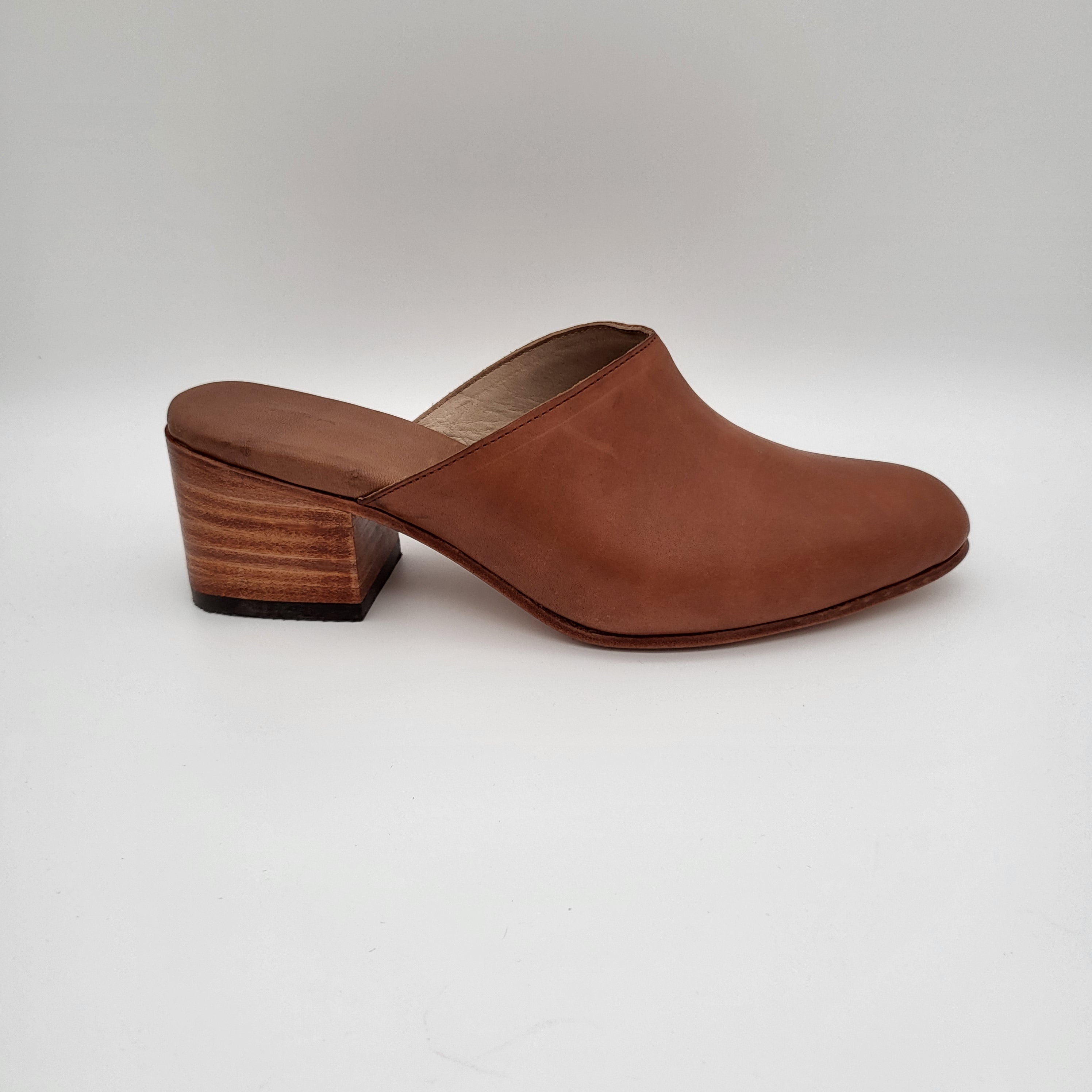 Ein brauner Lederslipper mit geschlossener Zehenpartie und einem klobigen, mittelhohen Holzabsatz, fotografiert vor einem schlichten weißen Hintergrund.