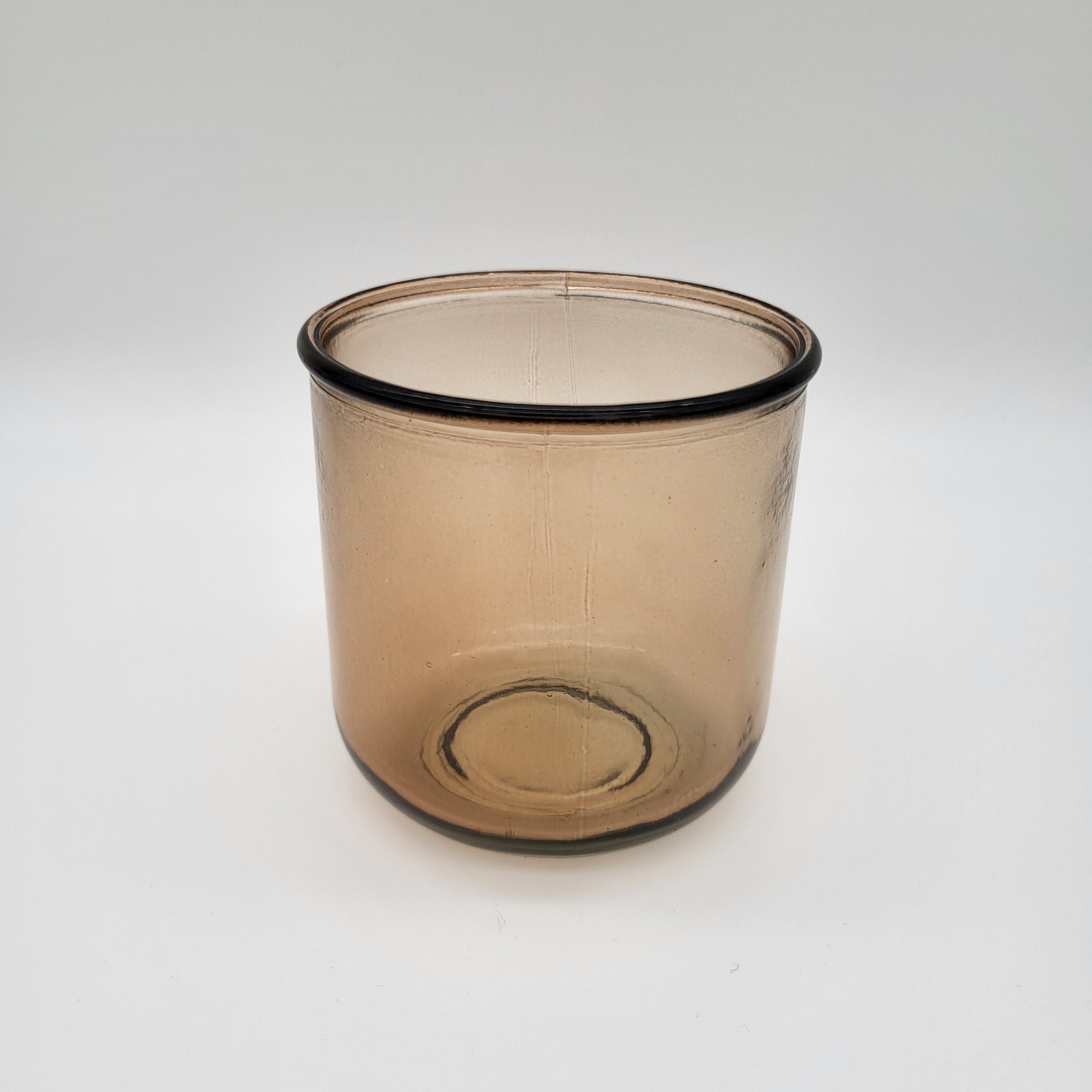 Ein durchscheinender, hellbrauner Glasbecher mit zylindrischer Form und glatter Oberfläche, fotografiert vor einem schlichten weißen Hintergrund.