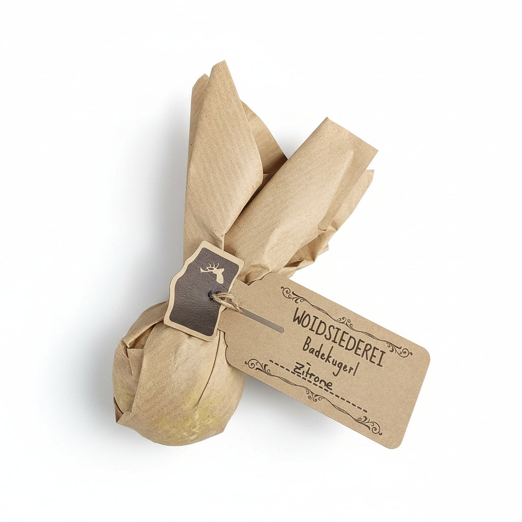 Eine runde, in braunes Papier eingewickelte Badebombe mit einem mit Schnur befestigten Anhänger mit der Aufschrift WOIDSIEDEREI Badekugel Zitrone auf weißem Hintergrund.