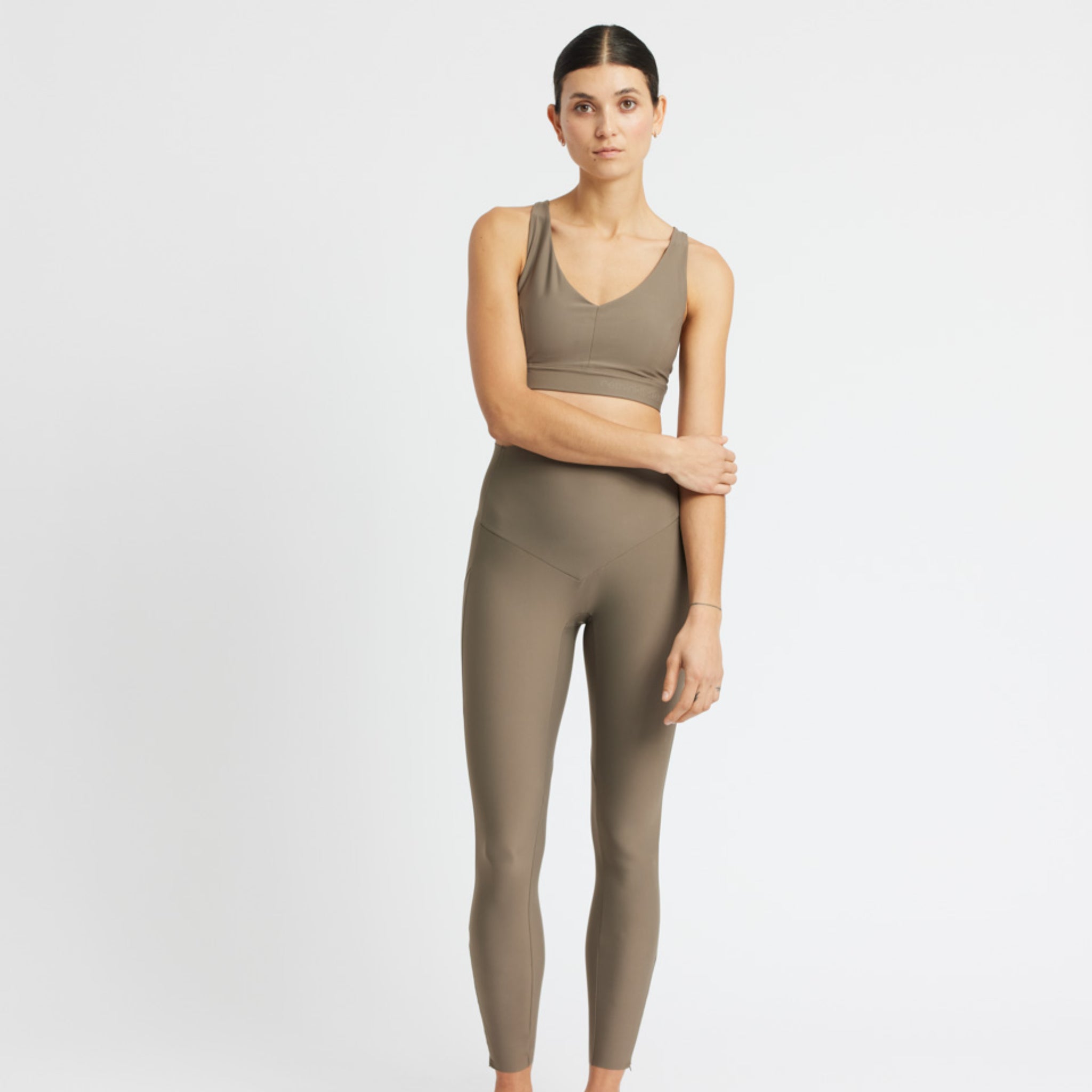 Frau in beige Sportbekleidung posiert vor einem weißen Hintergrund.