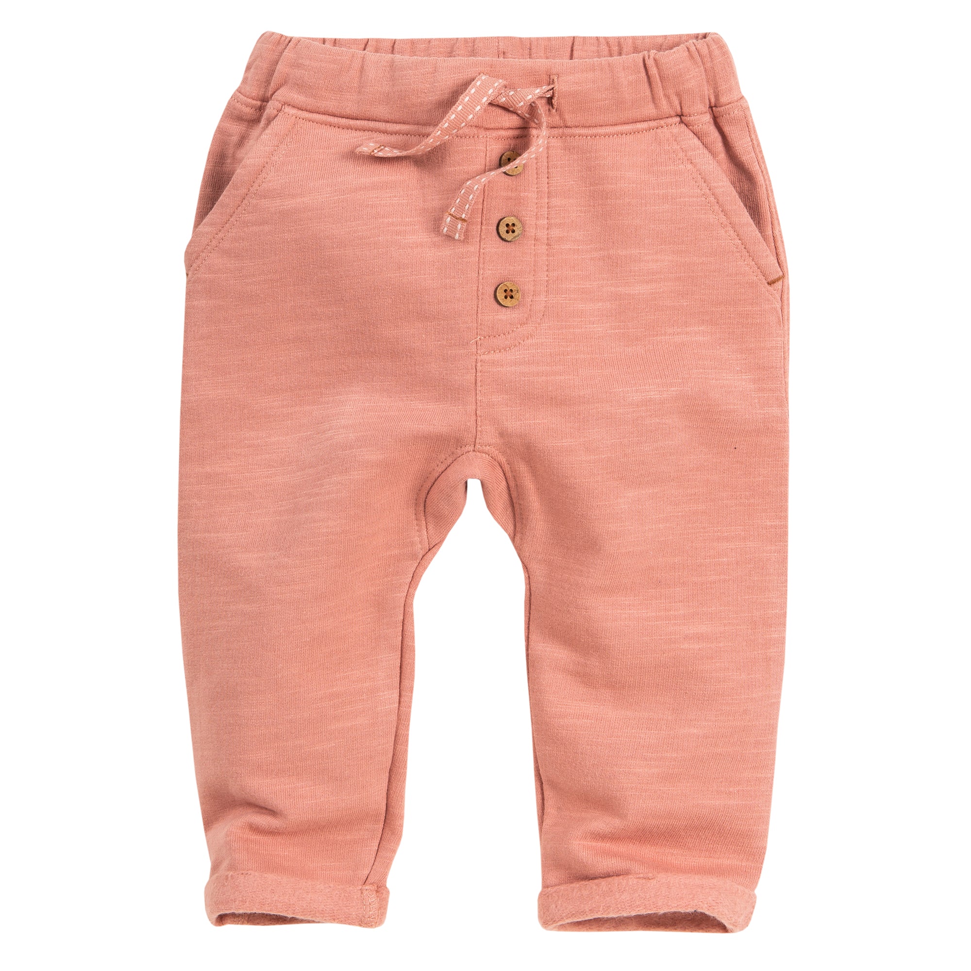 Pfirsichfarbene Babyhose mit elastischem Bund, Vordertaschen, dekorativem Kordelzug, zwei braunen Knöpfen und aufgerollten Bündchen. Der Stoff wirkt weich und bequem.