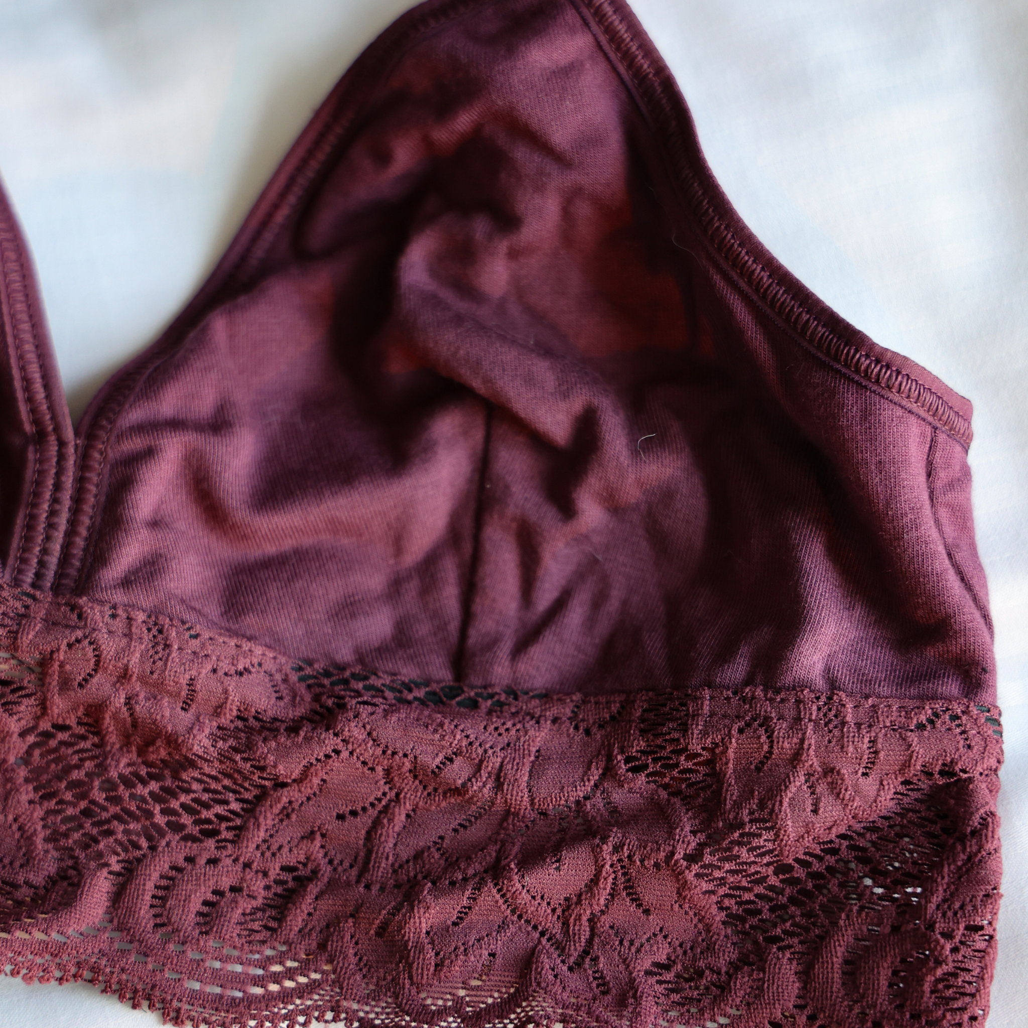 Nahaufnahme eines kastanienbraunen Bralettes mit Spitzenverzierung am unteren Rand, dargestellt auf einer hellen Fläche.