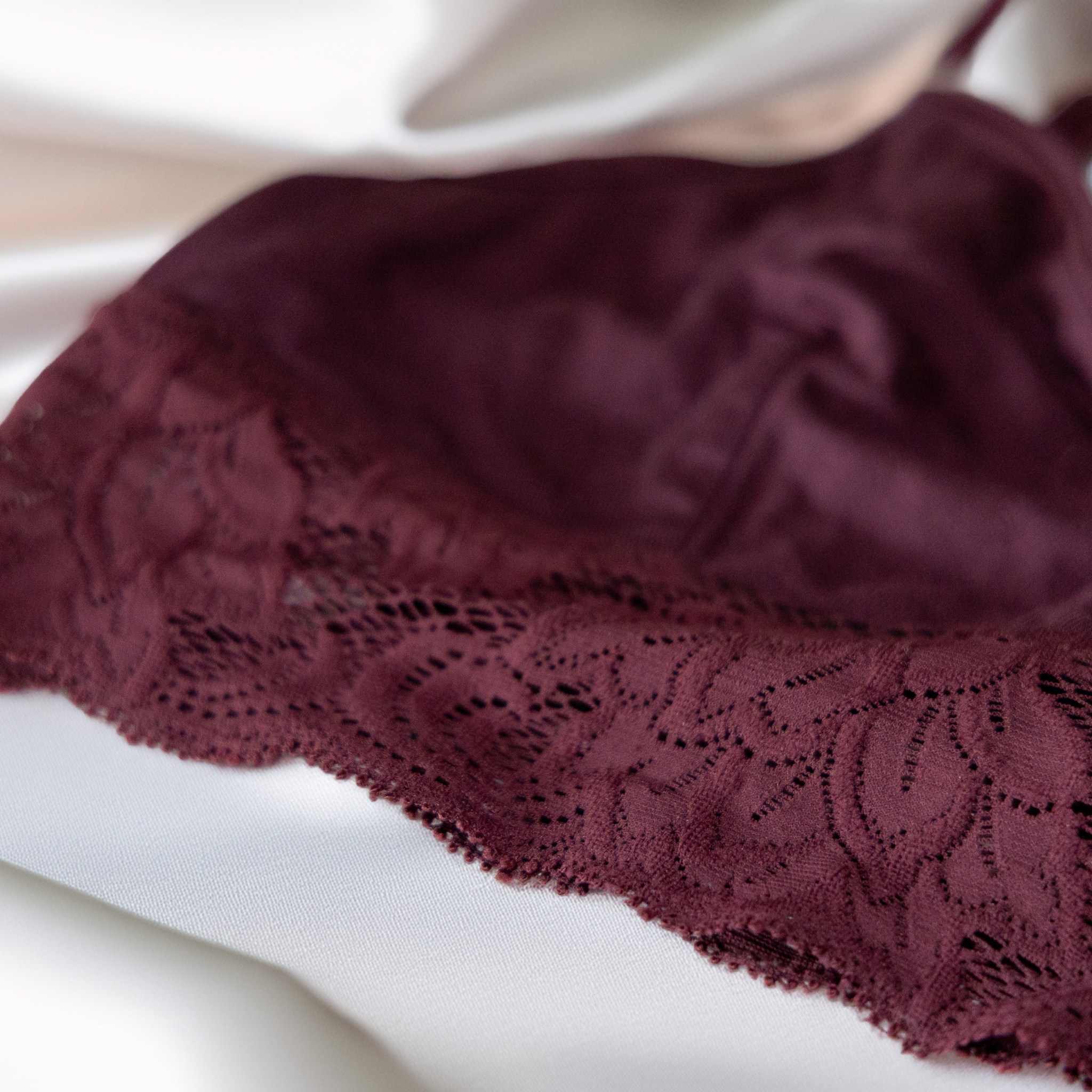 Eine Nahaufnahme eines burgunderroten Spitzen-Bralettes auf weißem Satinstoff.