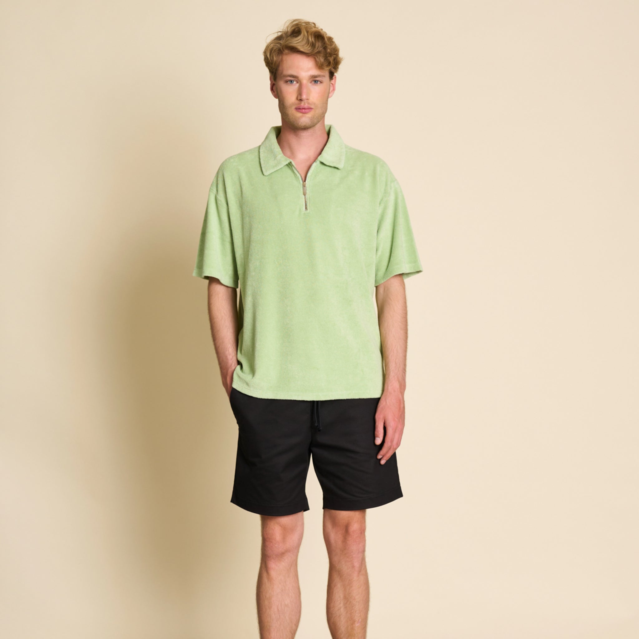 Mann in einem hellgrünen Polohemd und schwarzen Shorts steht vor einem hellen Hintergrund.